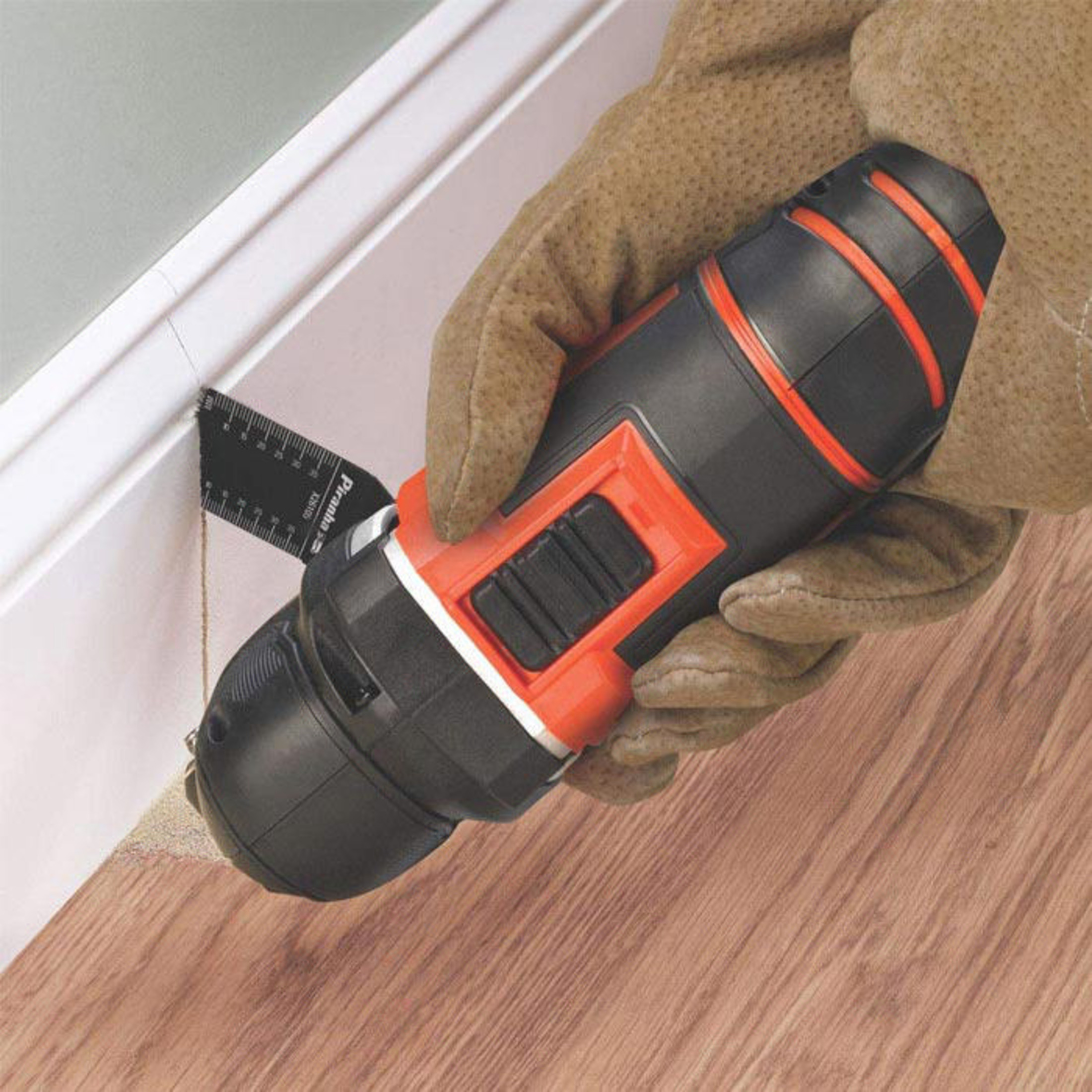 Ręka w brązowej rękawicy używa czarnego i pomarańczowego wiertła do białej listwy z linijką.