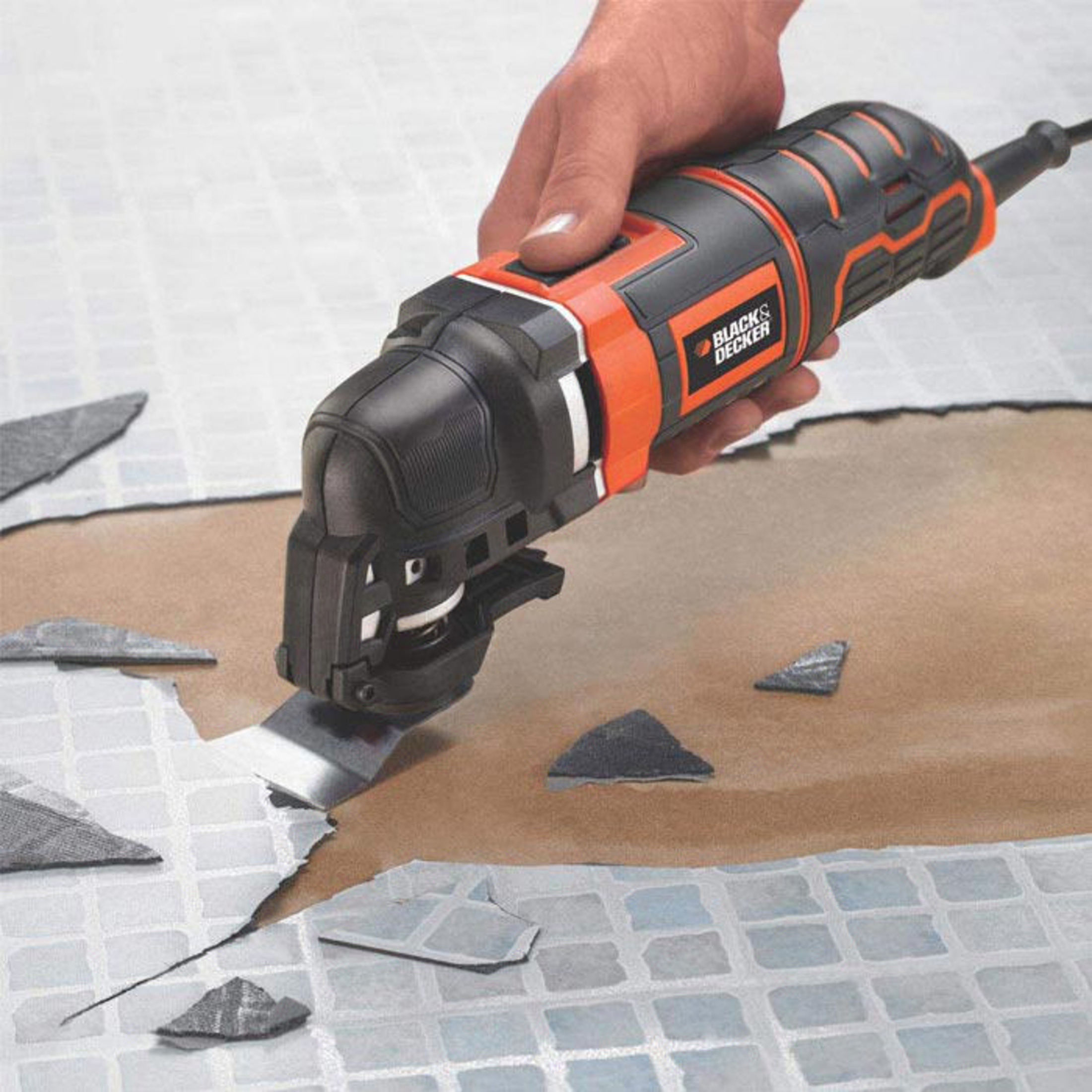 Ręka trzyma czarno-pomarańczowe narzędzie wielofunkcyjne usuwające płytki.