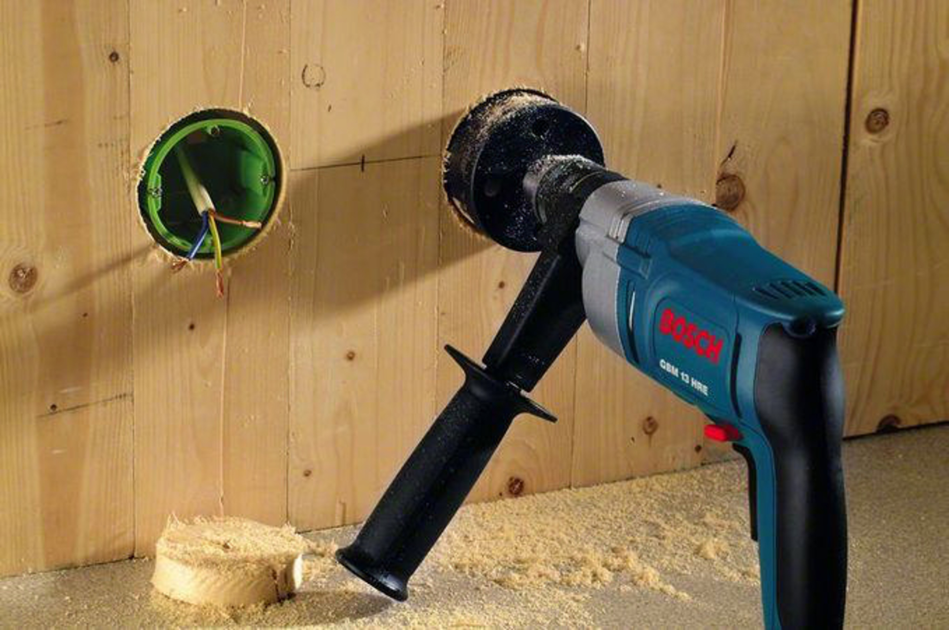 Trapano crea foro nel legno; fili e scatola visibili.