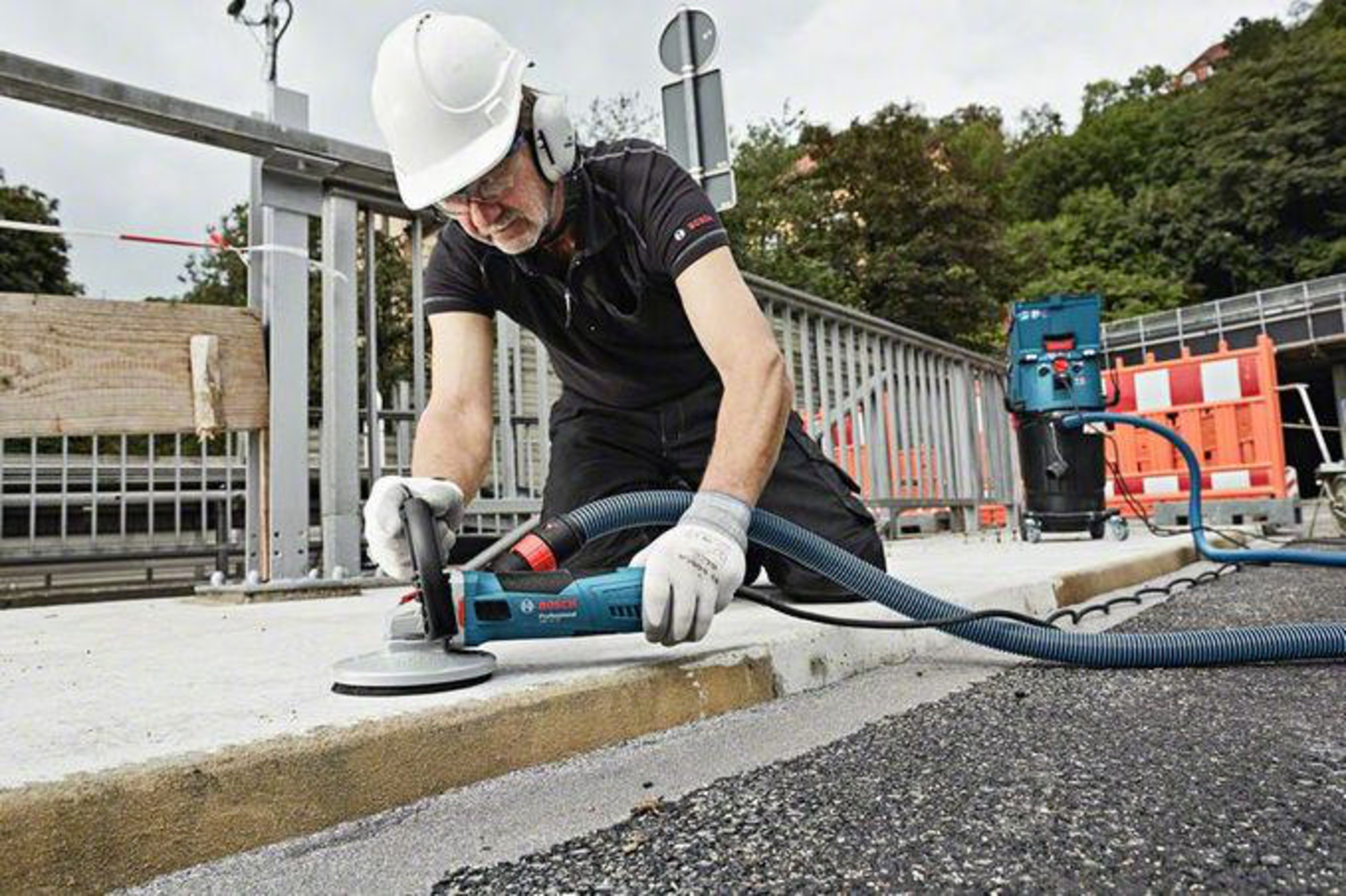 Mann schleift Beton mit Maschine, Staubabsaugung im Einsatz.