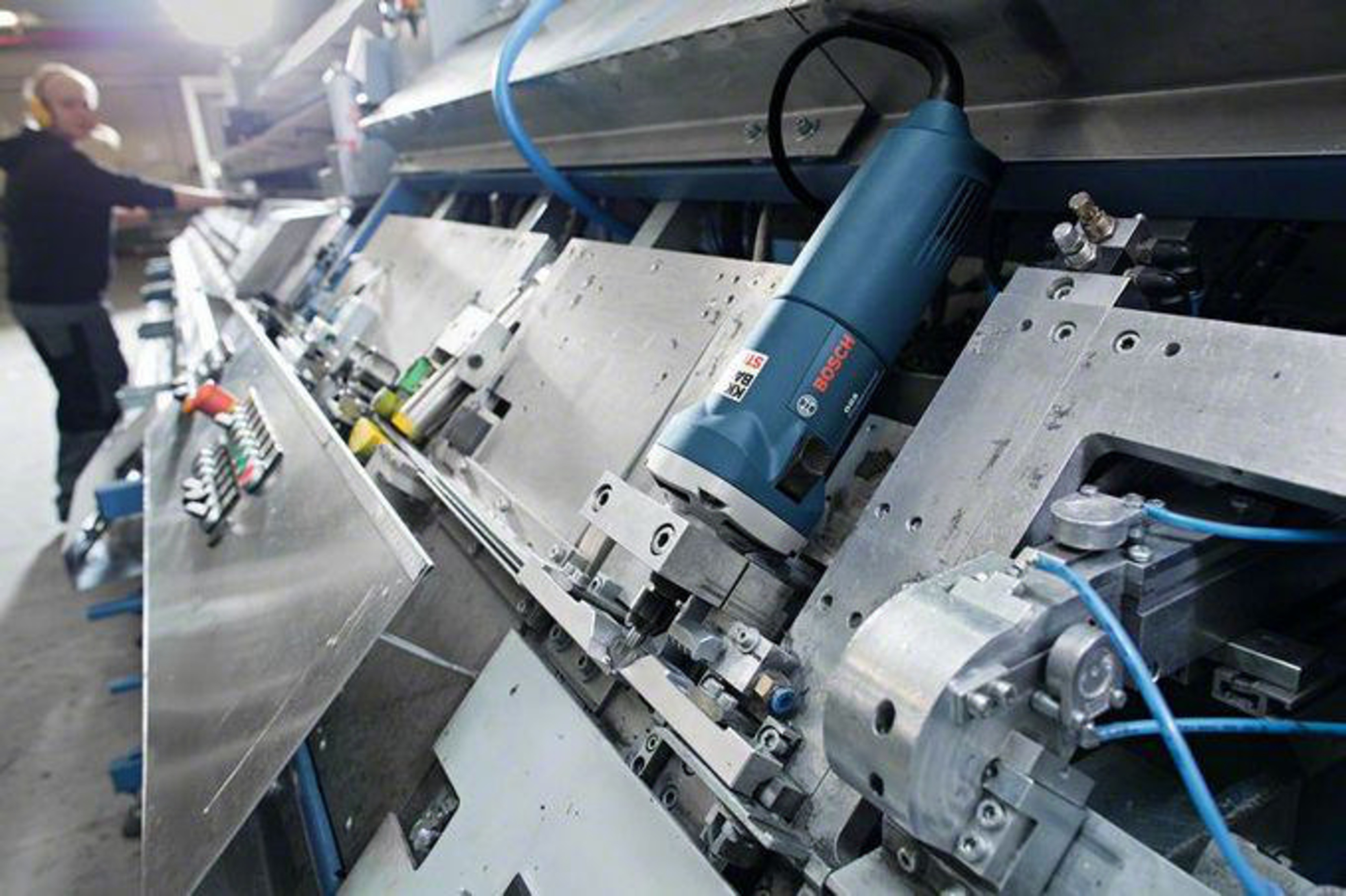 Un hombre en una fábrica opera una máquina con una herramienta azul.