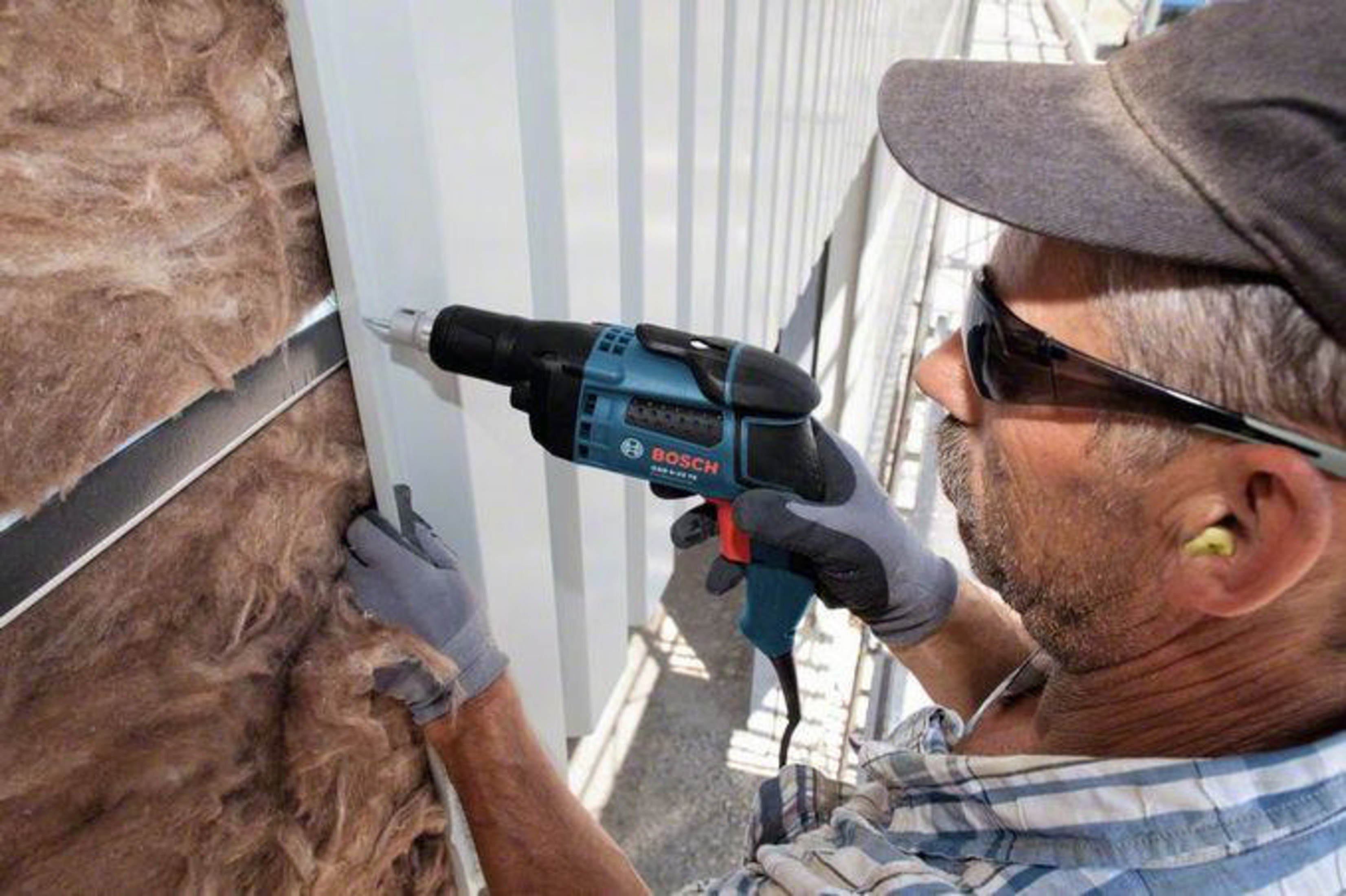 Hombre con taladro instala aislamiento junto a pared metálica.
