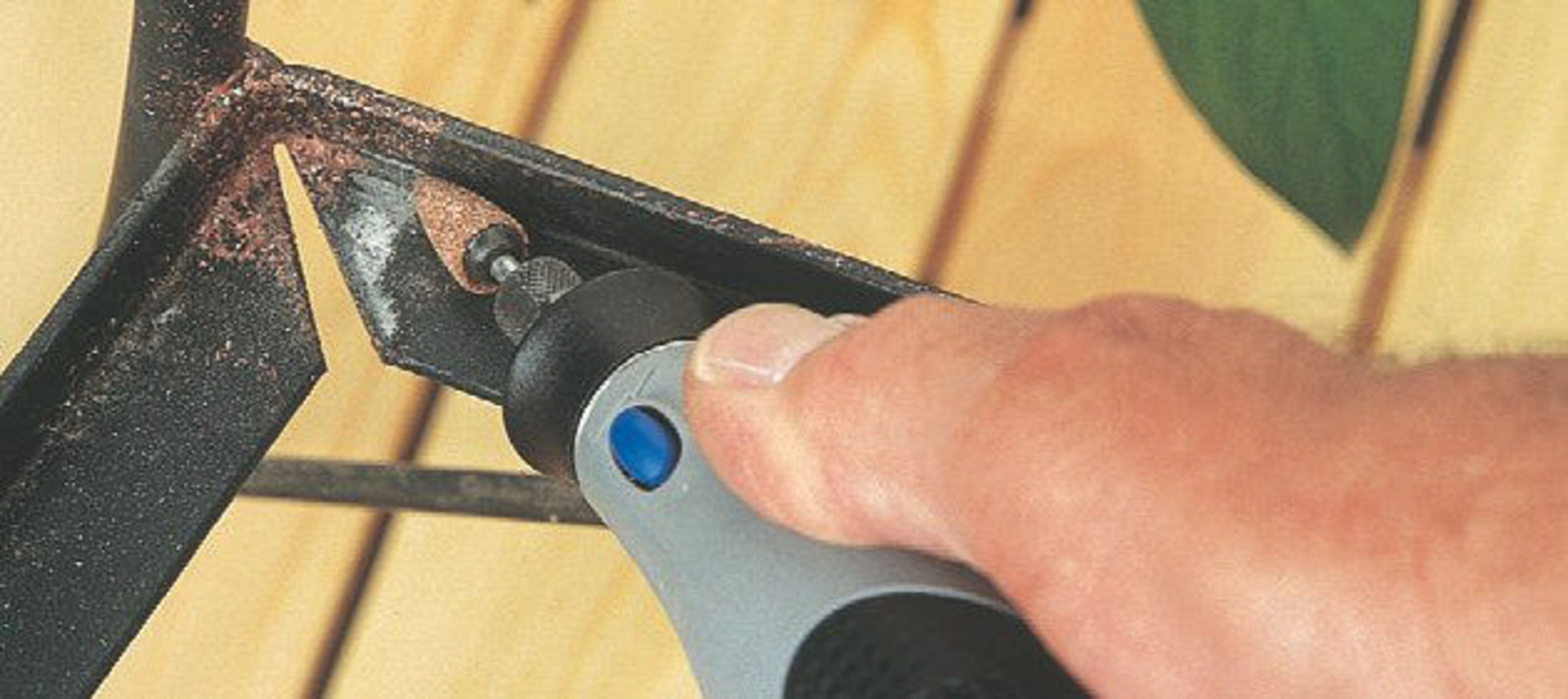 Hand met roterende tool schuurt roest op zwart metaal.
