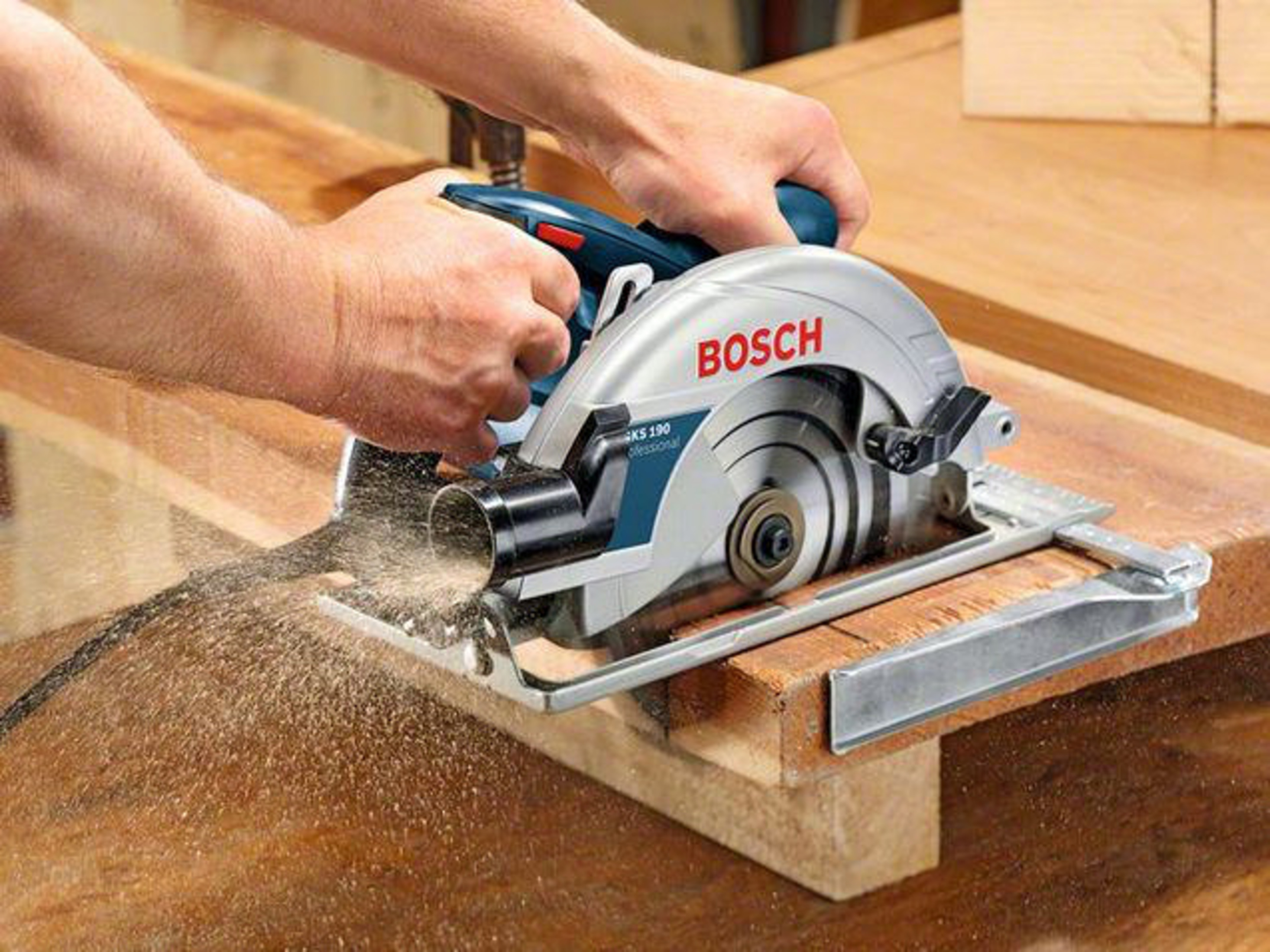 Eine Hand benutzt eine Bosch Kreissäge, um Holz zu schneiden. Sägespäne fliegen.