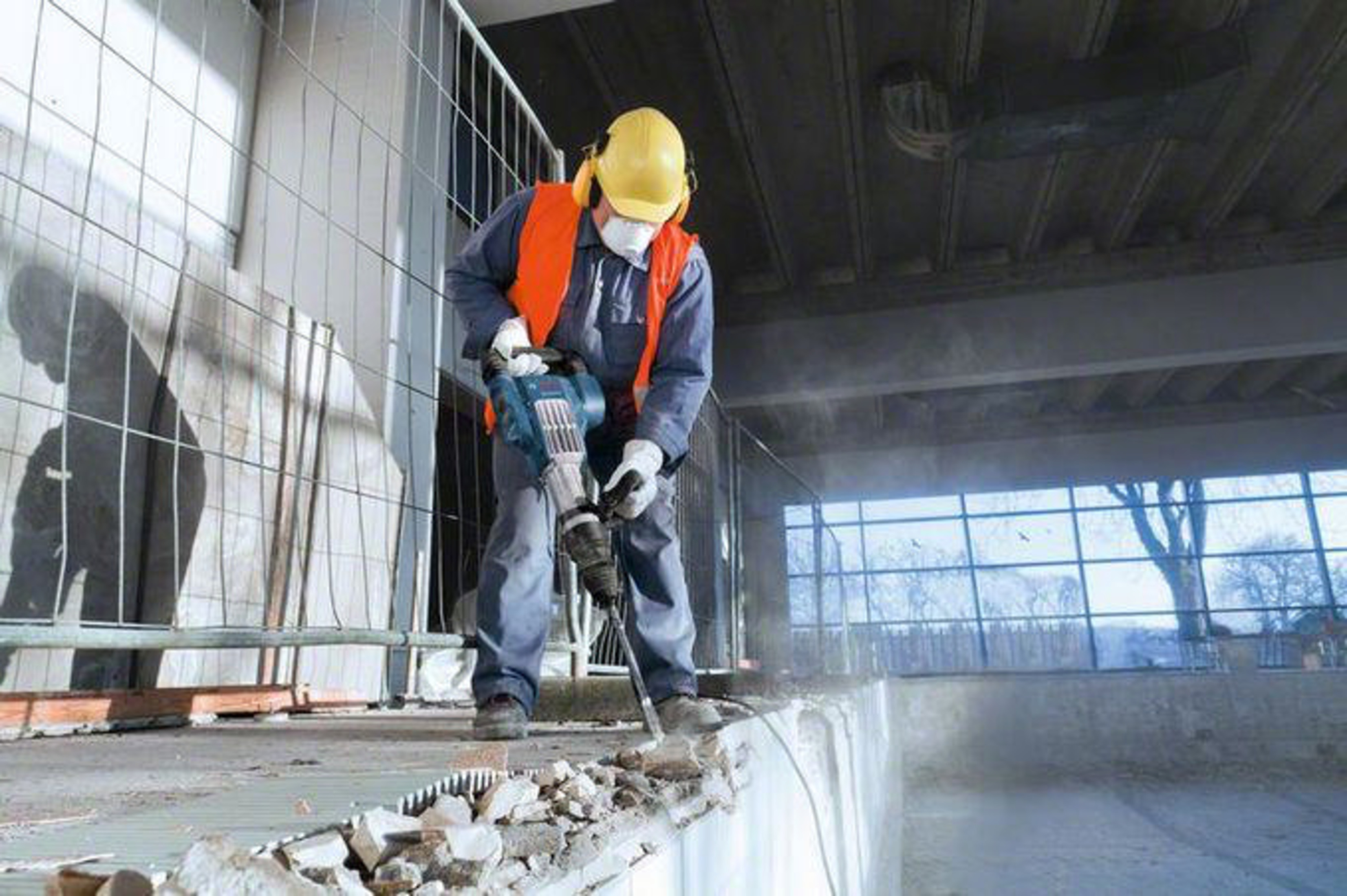 Mann mit Presslufthammer auf Baustelle, zerbricht Betonwand.