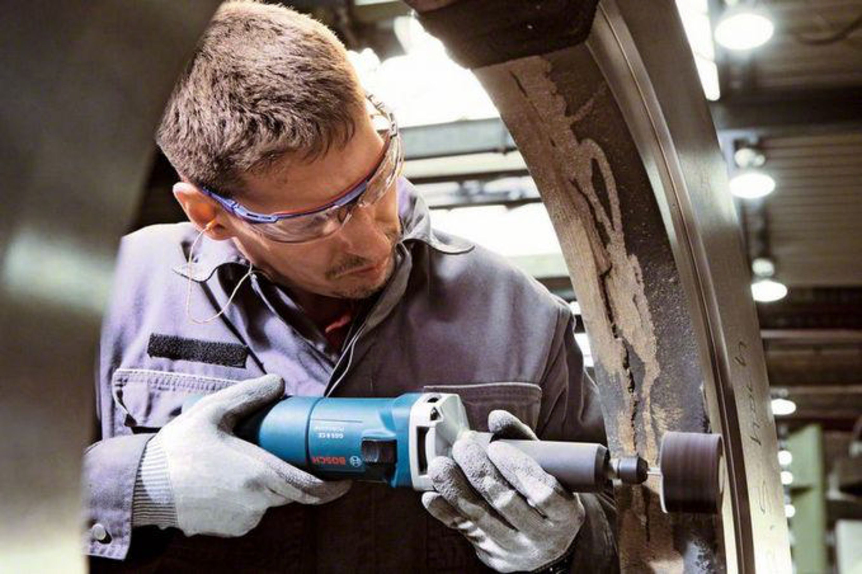 Mężczyzna w okularach ochronnych szlifuje metal niebieskim narzędziem Bosch.