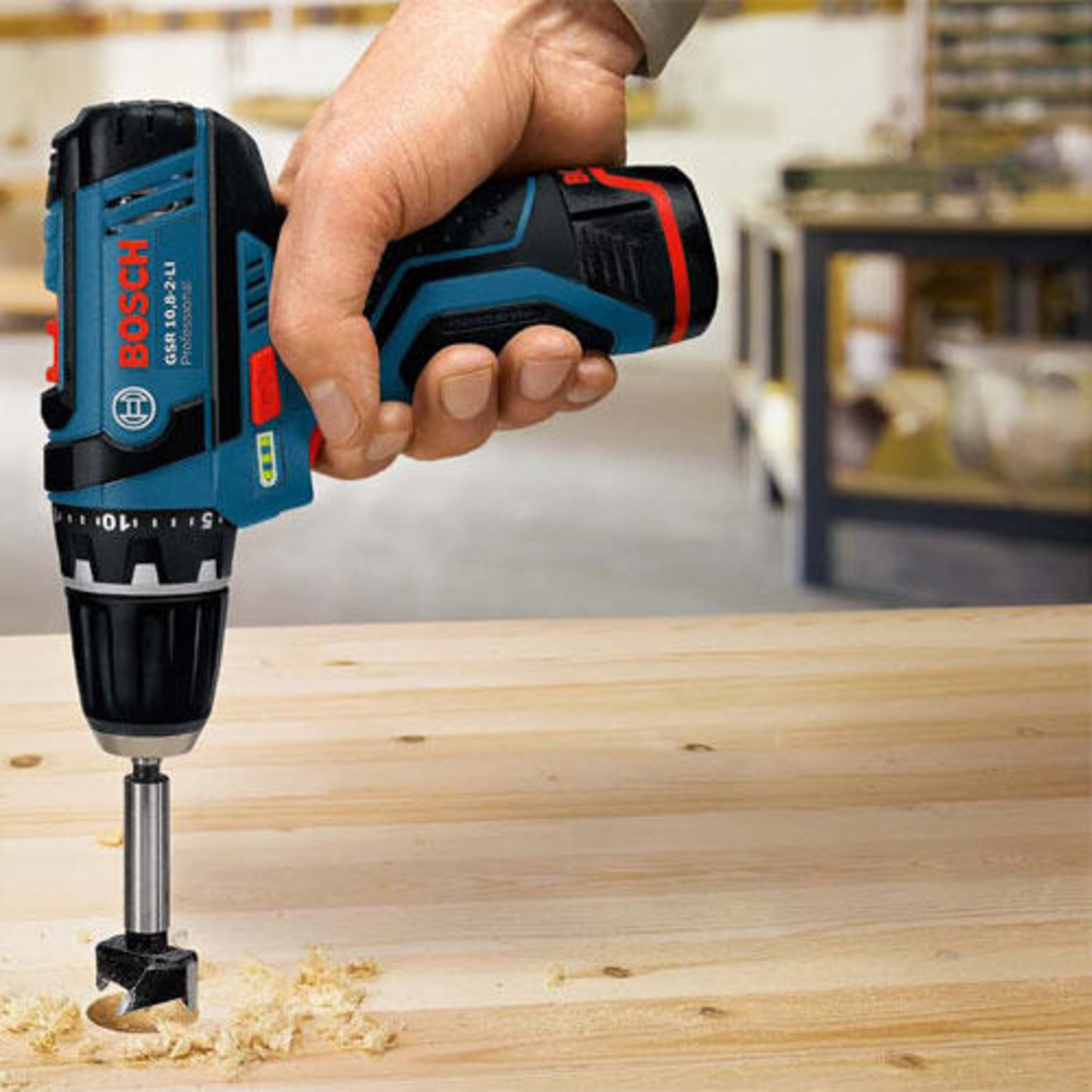 Eine Hand hält einen blauen Bosch-Akkuschrauber, der in Holz bohrt.
