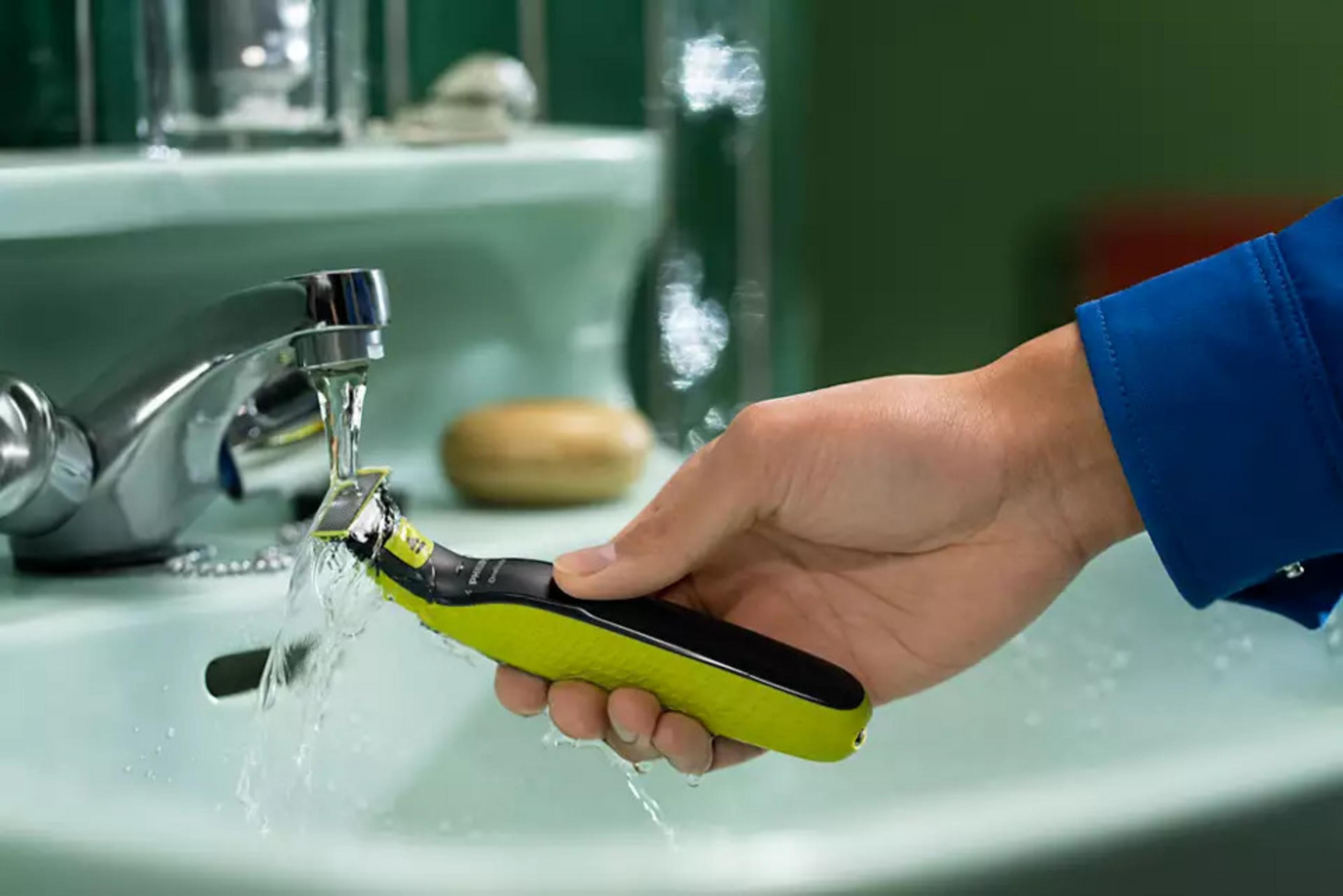 Un rifinitore verde viene sciacquato sotto l'acqua corrente in un lavandino.