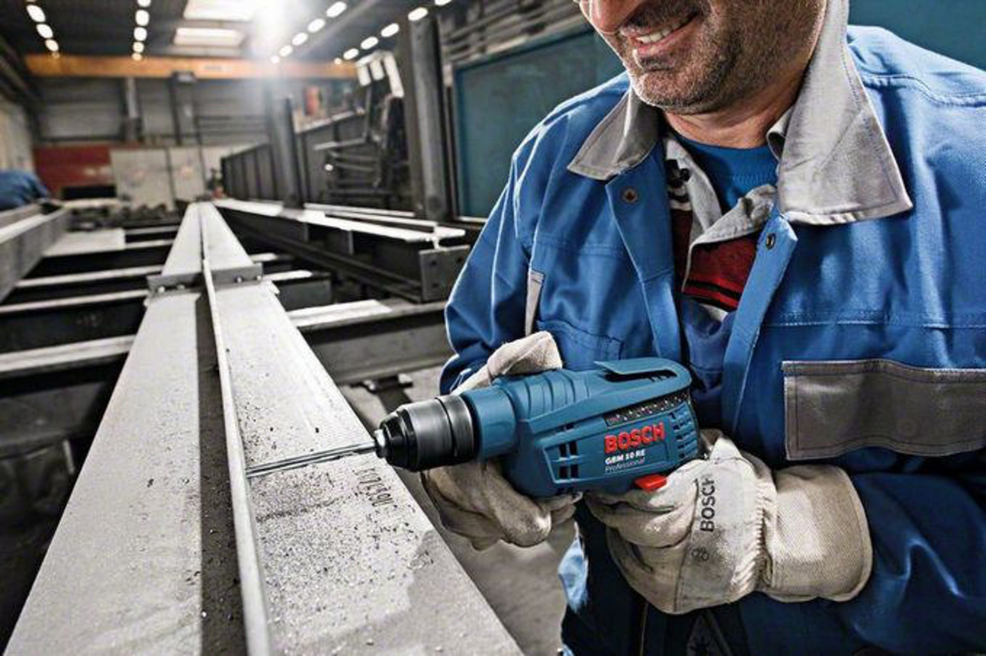 Un hombre con ropa de trabajo azul perfora una viga de metal.