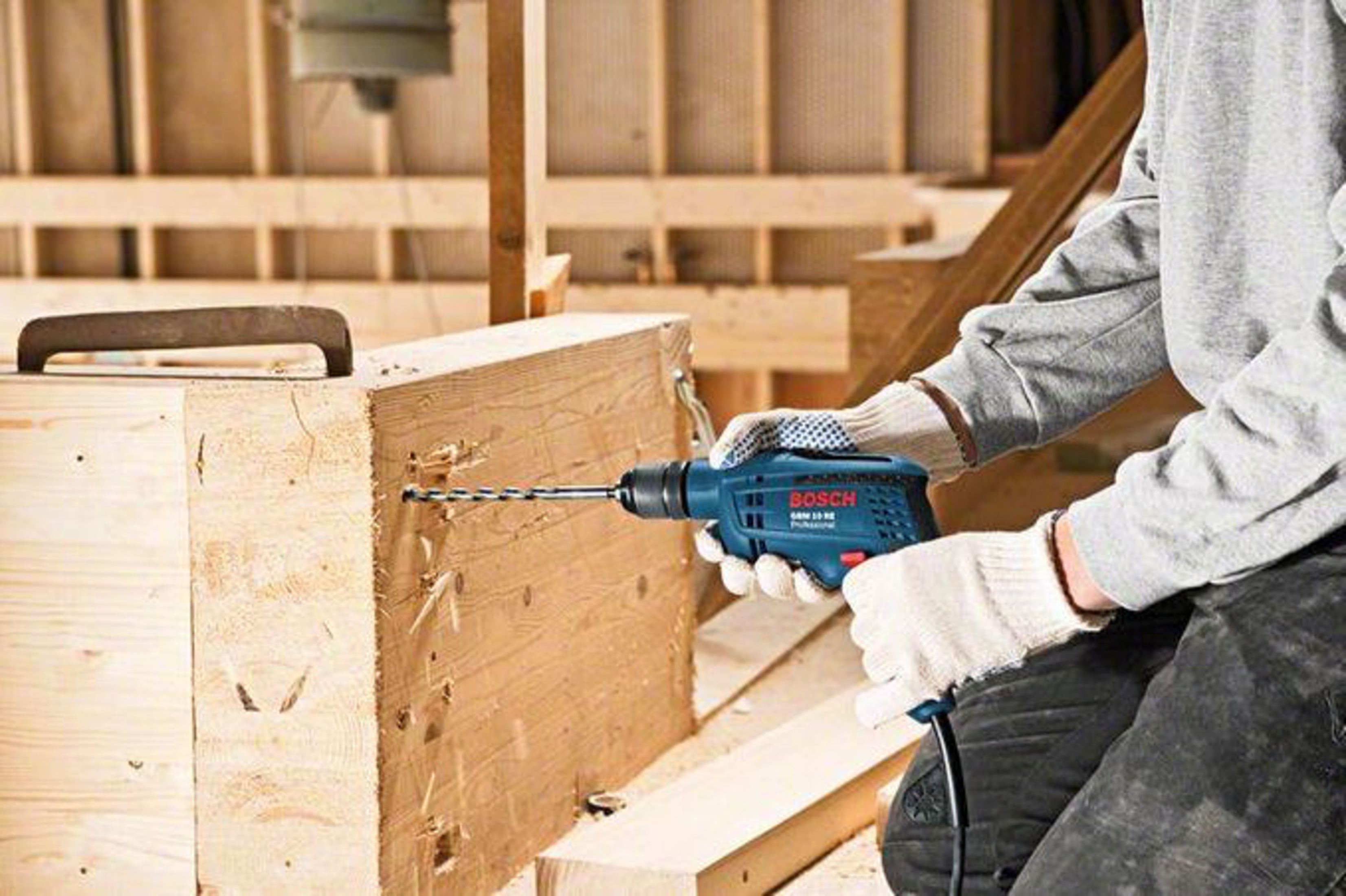 Un hombre taladra un trozo de madera con un taladro Bosch azul.