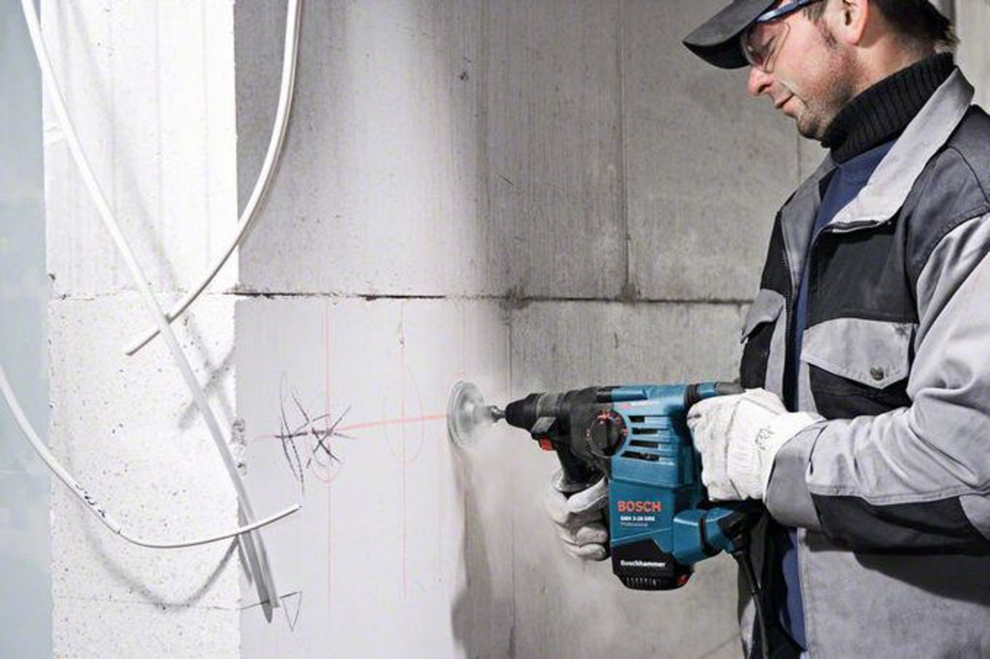Güvenlik gözlüklü ve iş kıyafetli bir adam, kırmızı lazer çizgileri görünen beton duvarda Bosch kırıcı delici kullanıyor.