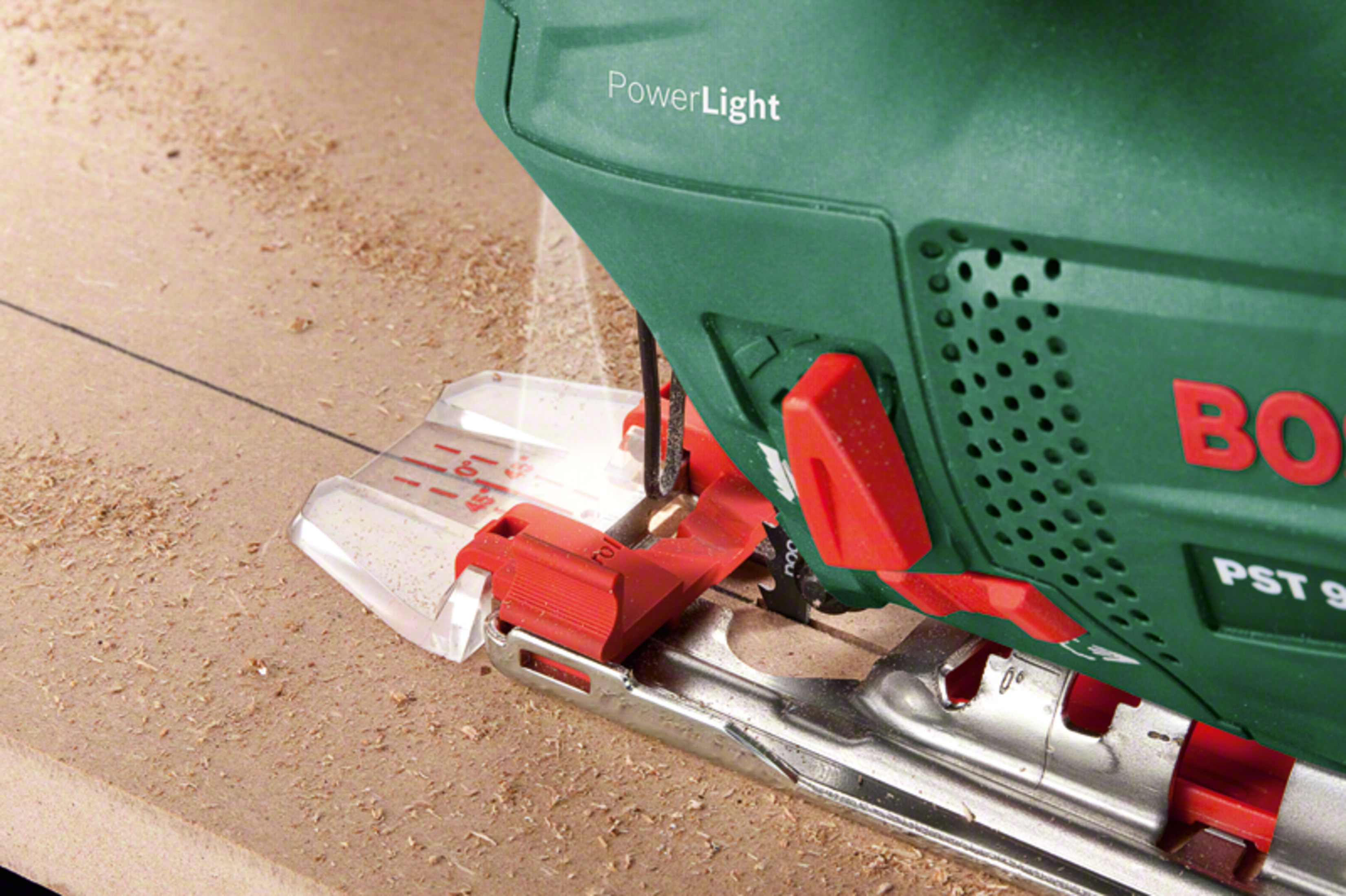 Zielona wyrzynarka Bosch tnie drewno. Wióry są rozsypane.