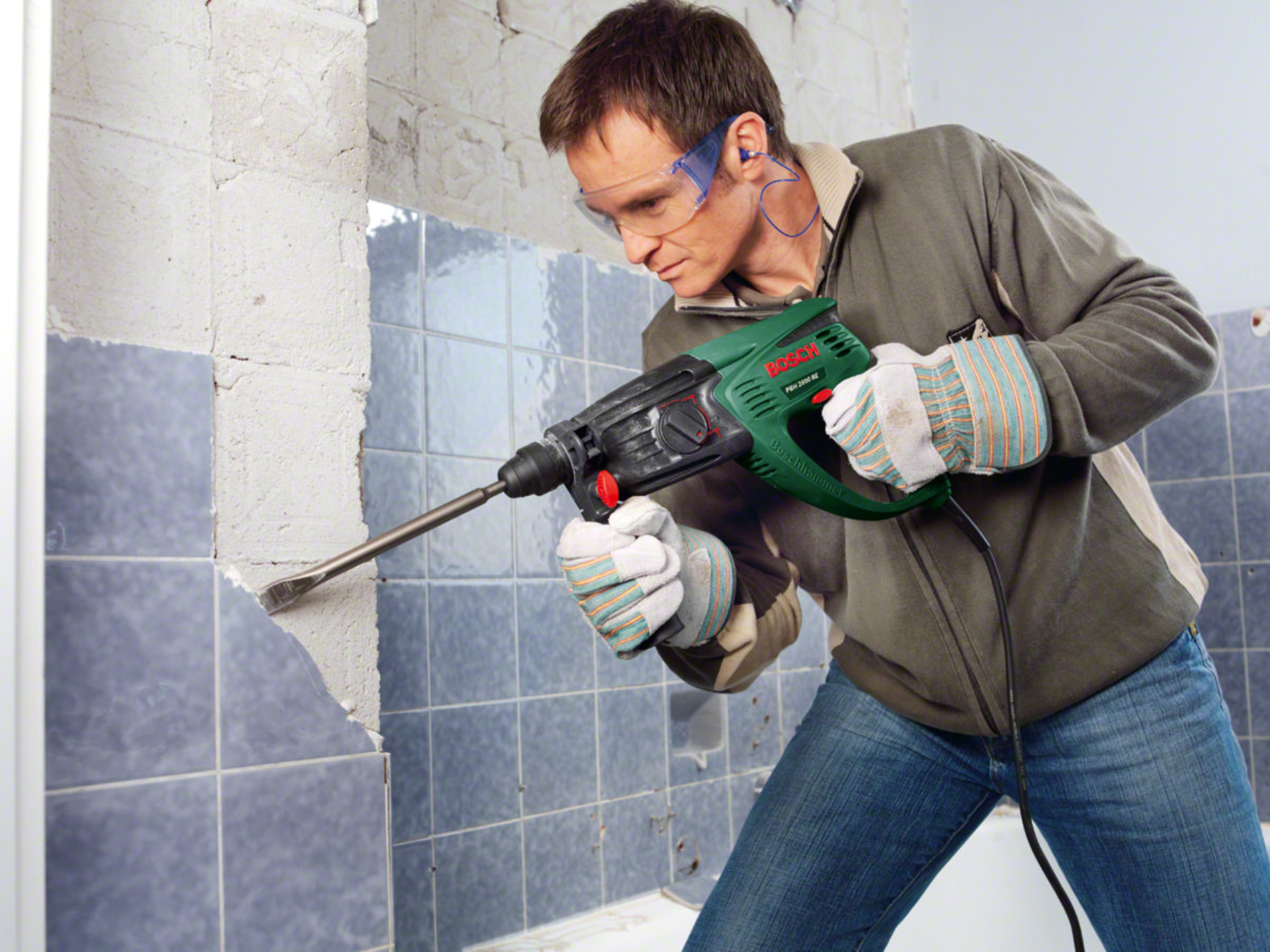 Mann mit Bohrhammer entfernt Fliesen von einer Wand.