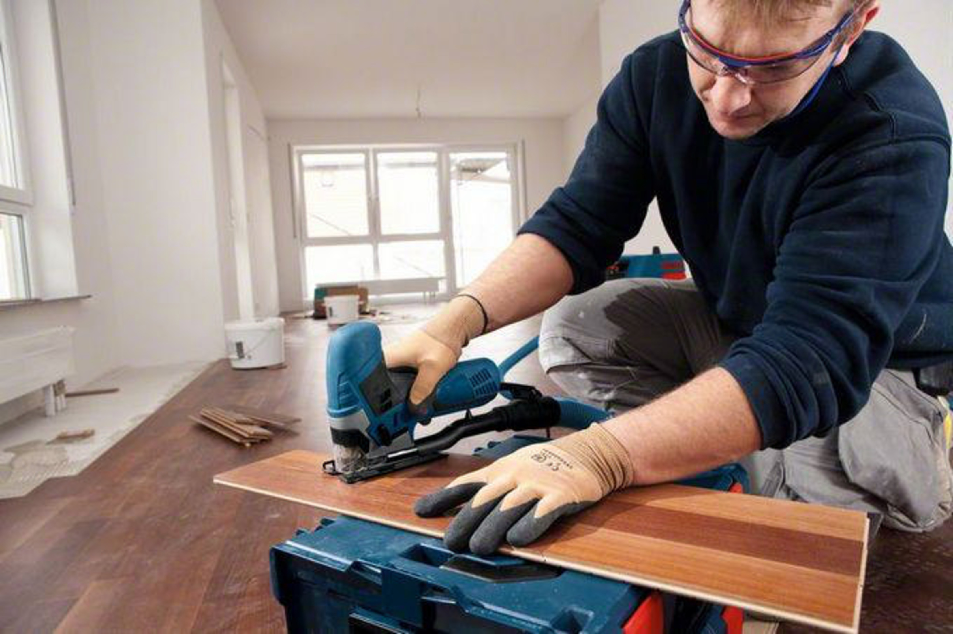 Mężczyzna w okularach ochronnych używa wyrzynarki do cięcia desek na skrzynce.