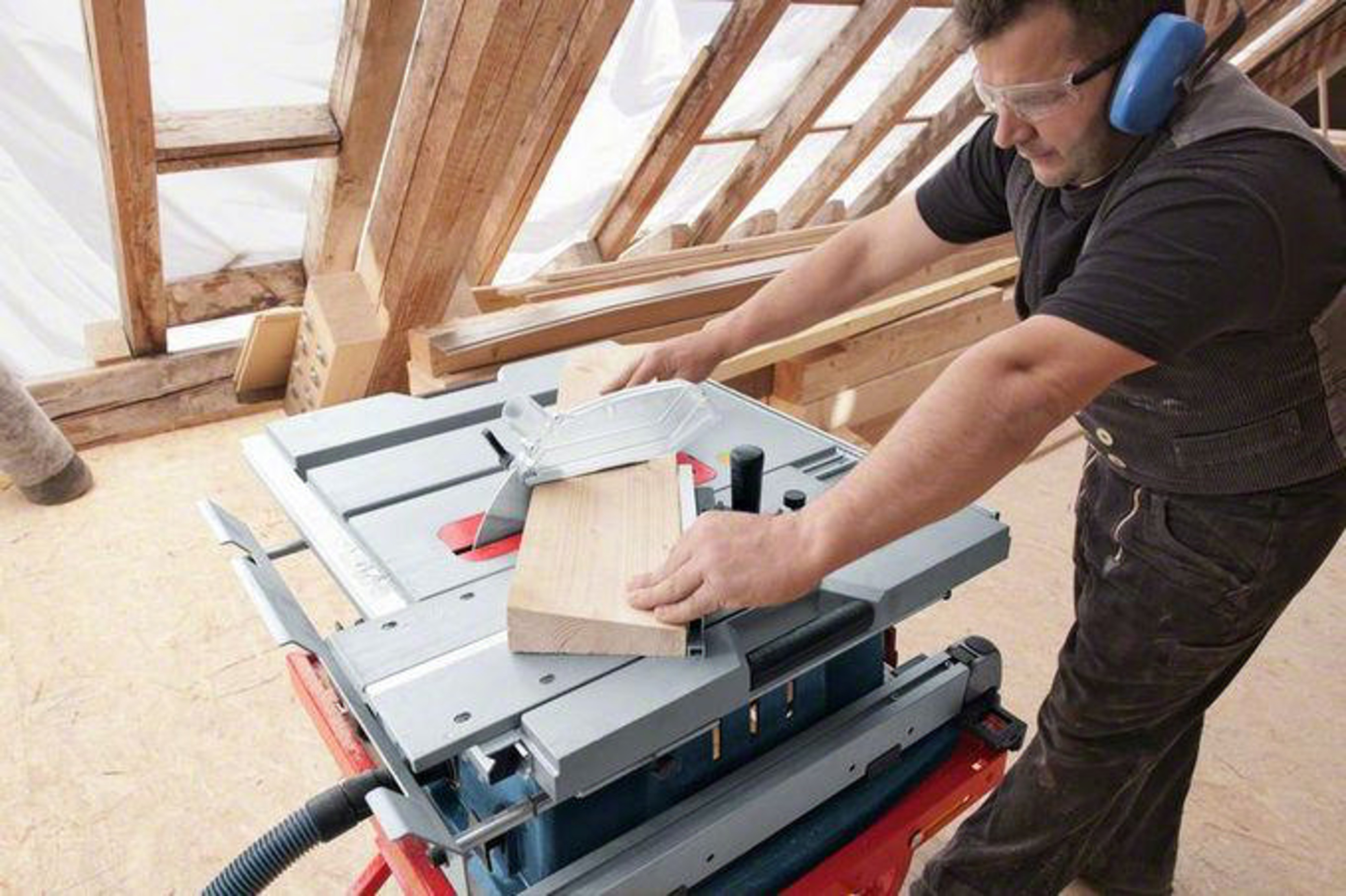 Uomo taglia legno con sega da banco, indossa protezioni.
