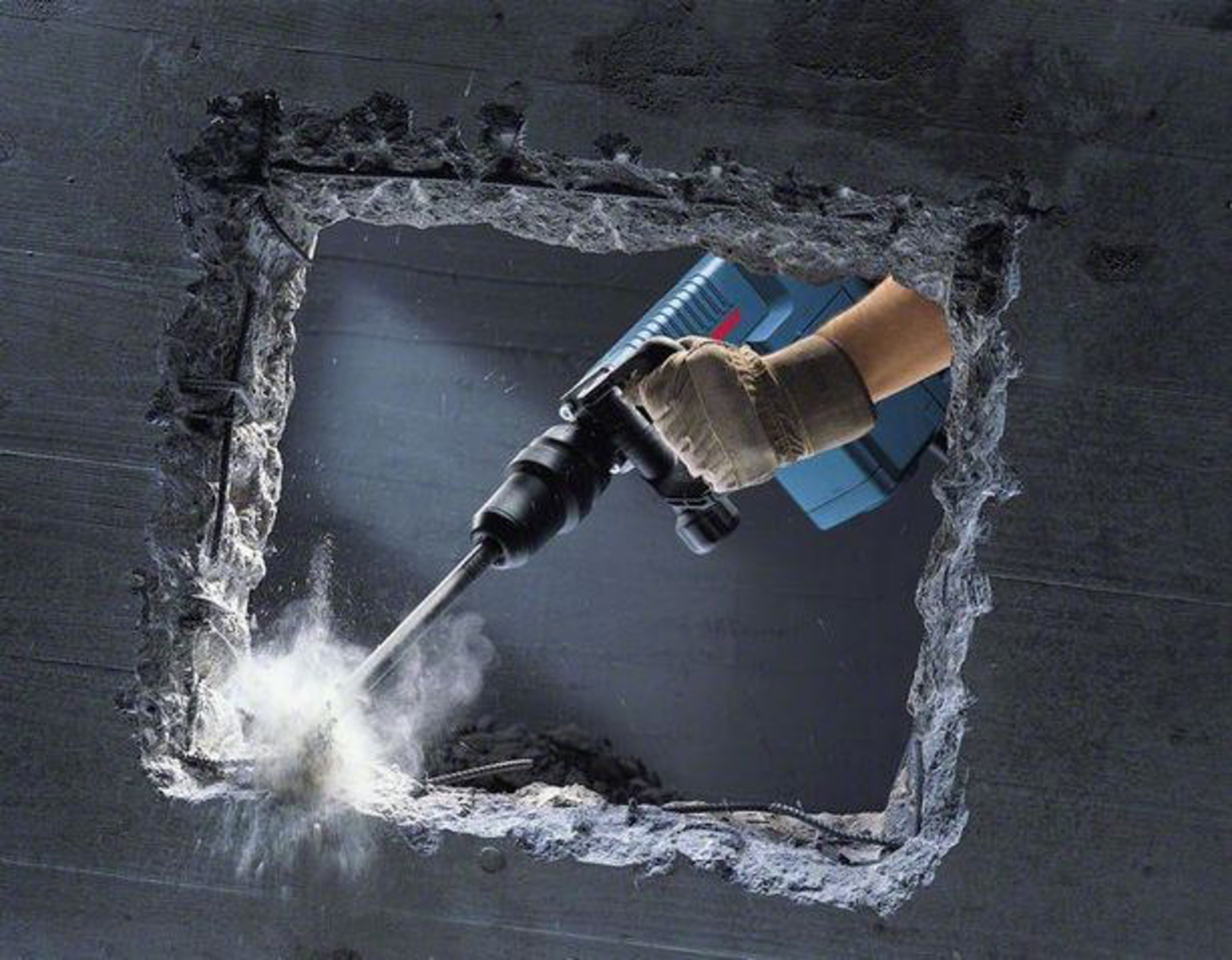 Un martello demolitore attraversa il cemento, sollevando polvere.