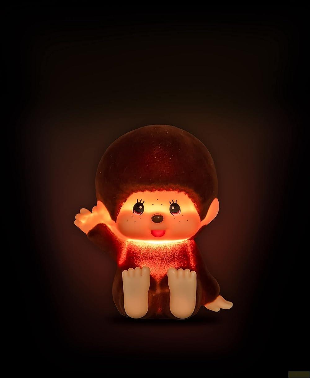 Ein beleuchtetes Monchhichi-Spielzeug sitzt im Dunkeln und winkt.