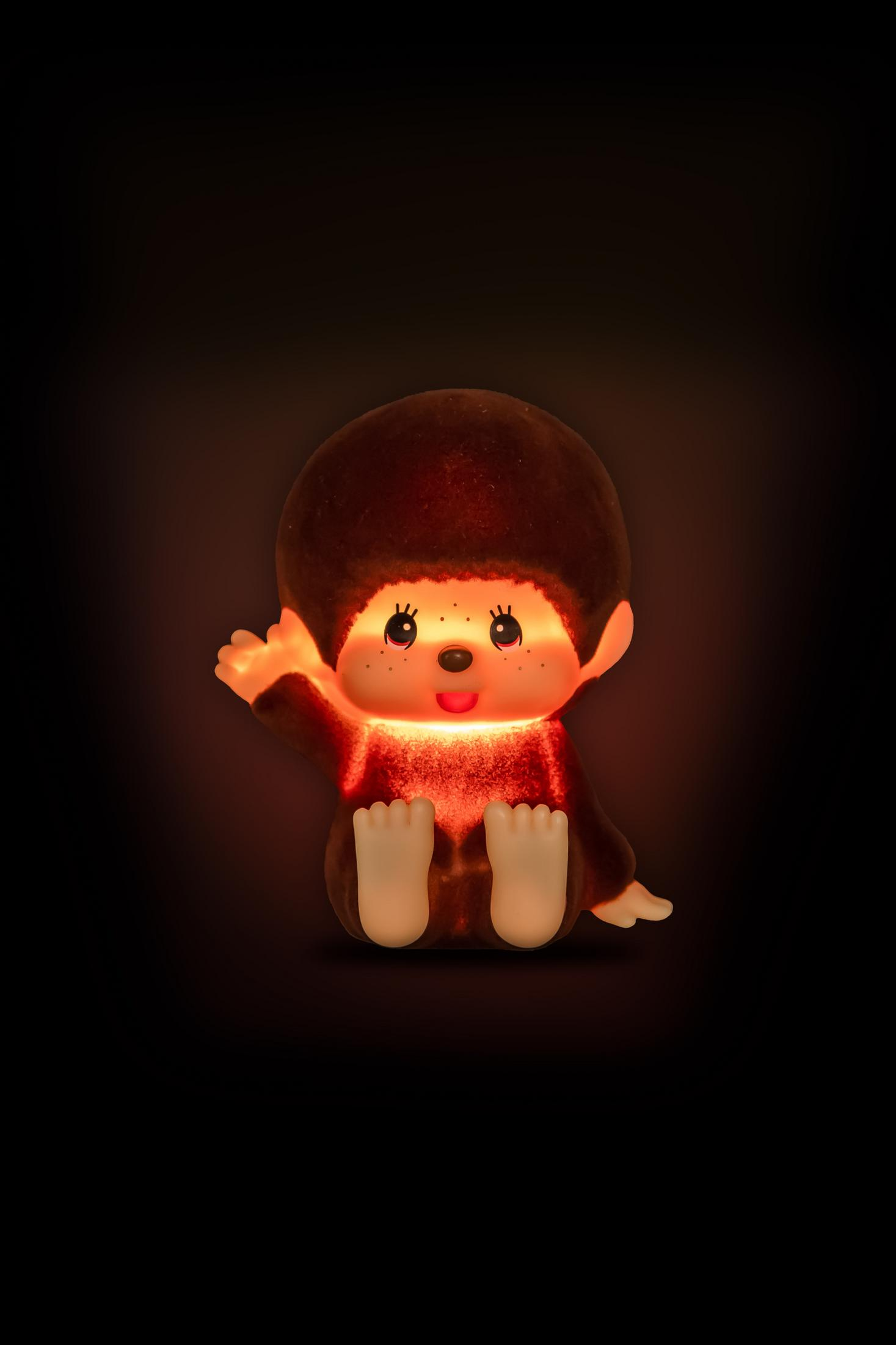 Ein leuchtendes Monchhichi-Spielzeug winkt in dunkler Umgebung.