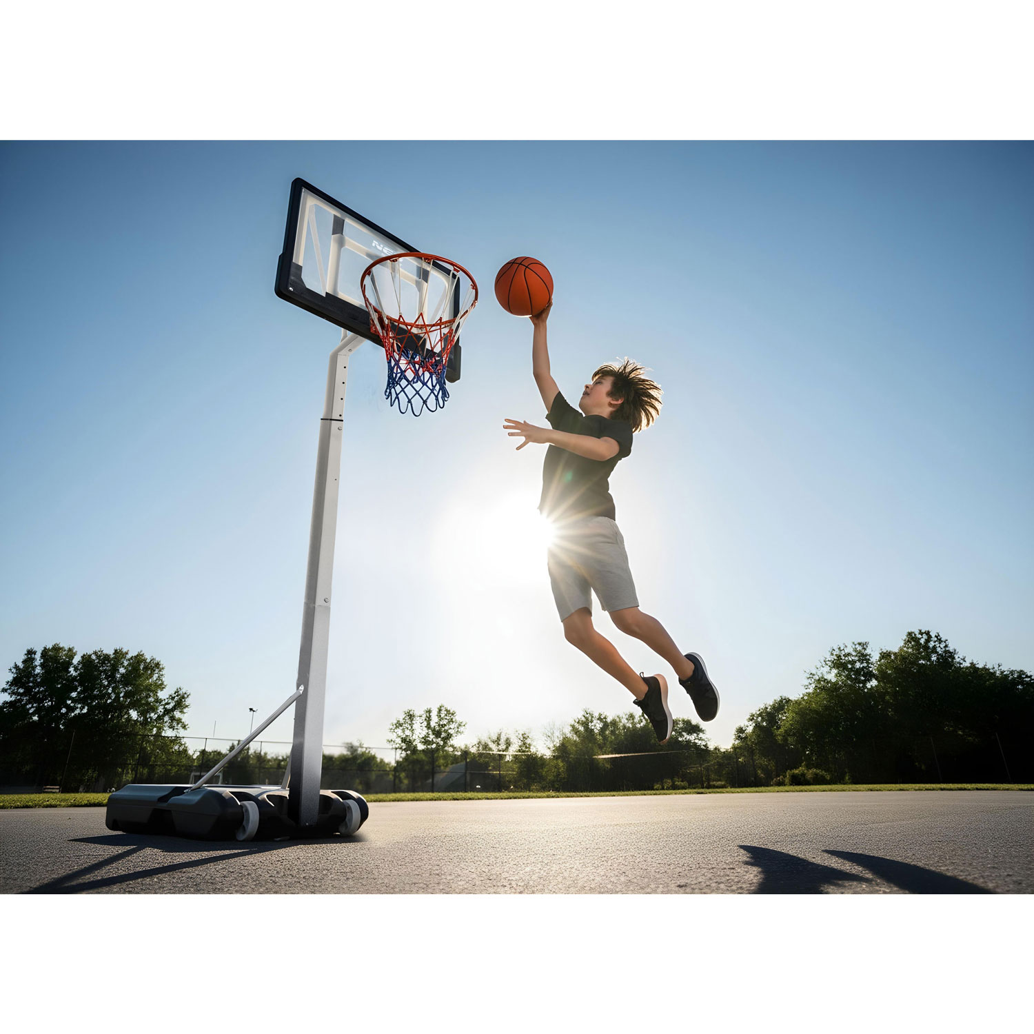 Chłopiec skacze, by rzucić piłkę do kosza, ze słońcem za nim.