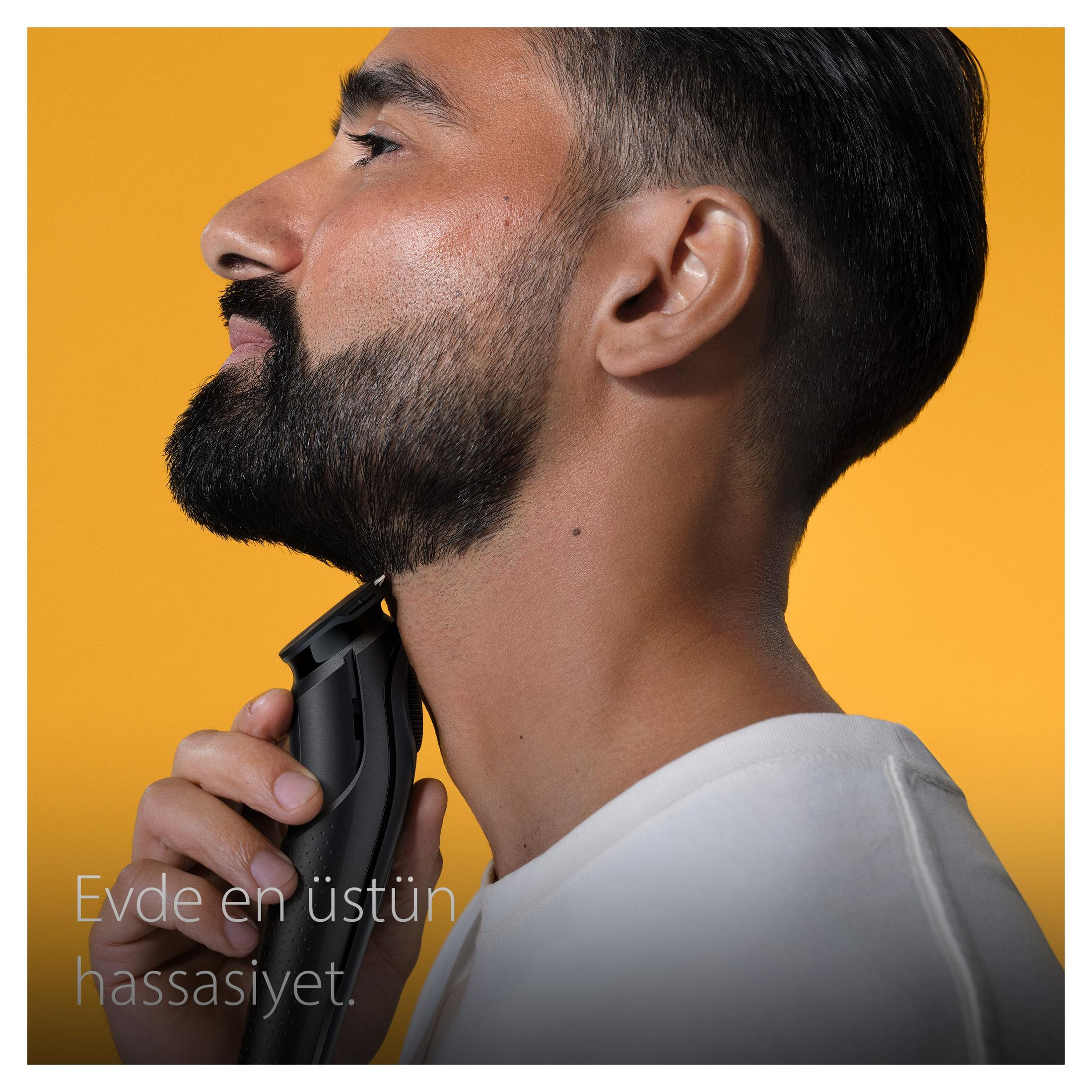 Uomo si taglia la barba con il trimmer su sfondo giallo.