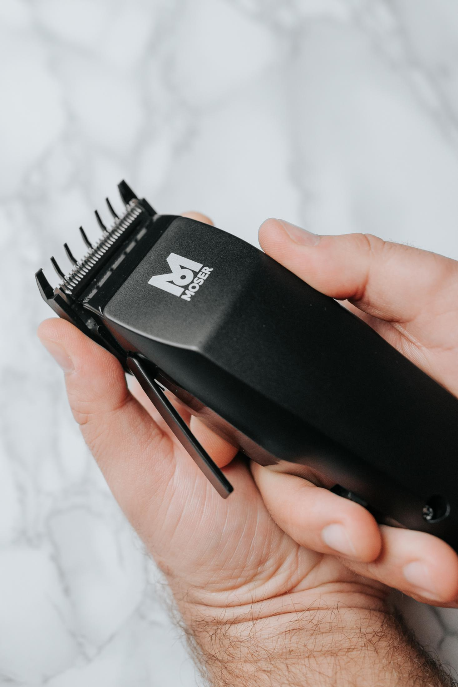 Osoba trzyma czarną maszynkę do strzyżenia Moser z logo M.