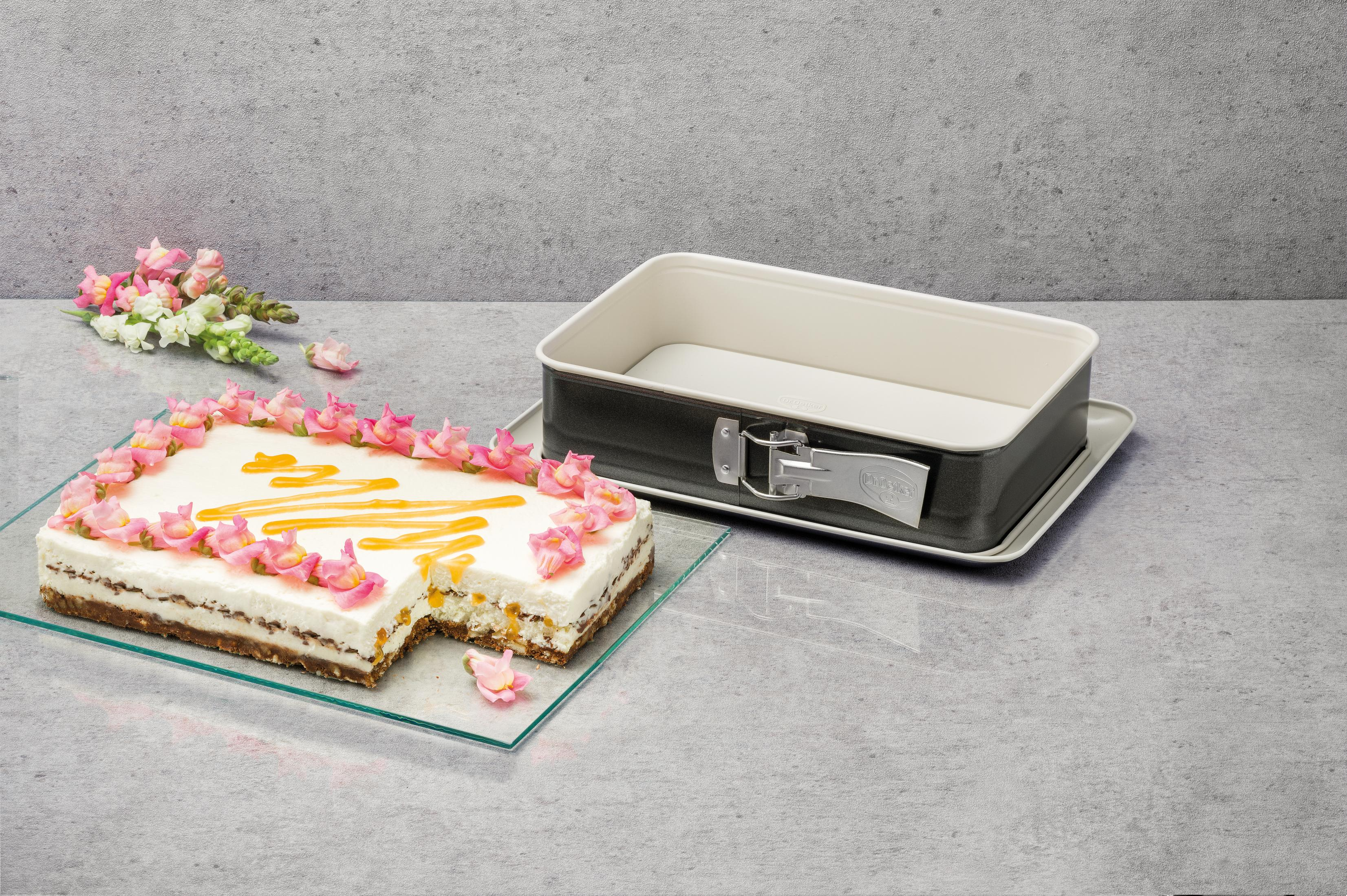 Kuchen mit weißen und rosa Blumen verziert, daneben eine Backform.