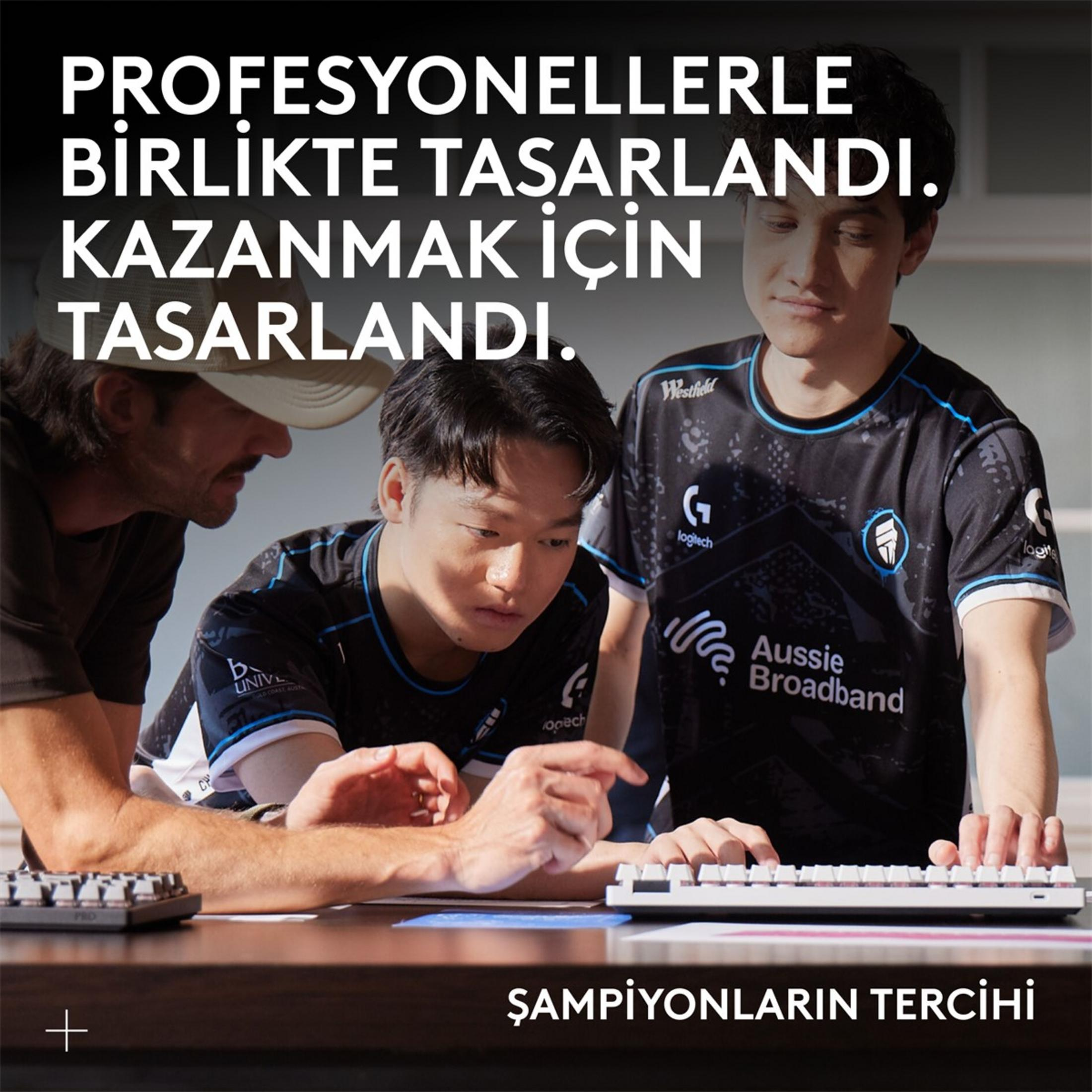 Trzech mężczyzn, dwóch w czarnych koszulkach e-sportowych, skupionych na klawiaturach przy biurku. Nakładka tekstowa: „ZAPROJEKTOWANO Z PROFESJONALISTAMI. ZAPROJEKTOWANO, ABY WYGRAĆ. WYBÓR MISTRZÓW.”