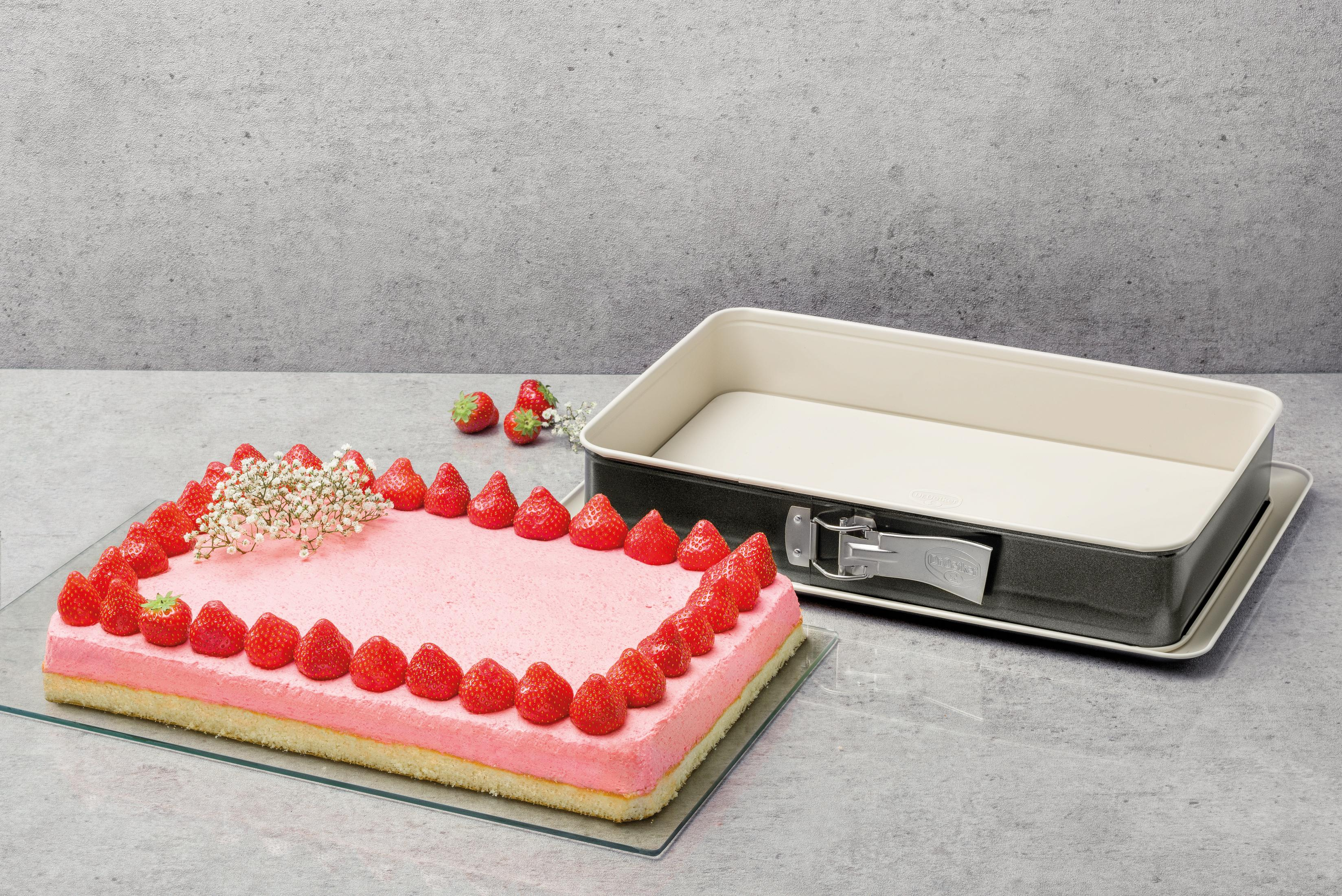 Ein rechteckiger Kuchen mit rosa Creme und Erdbeeren, daneben eine Backform.