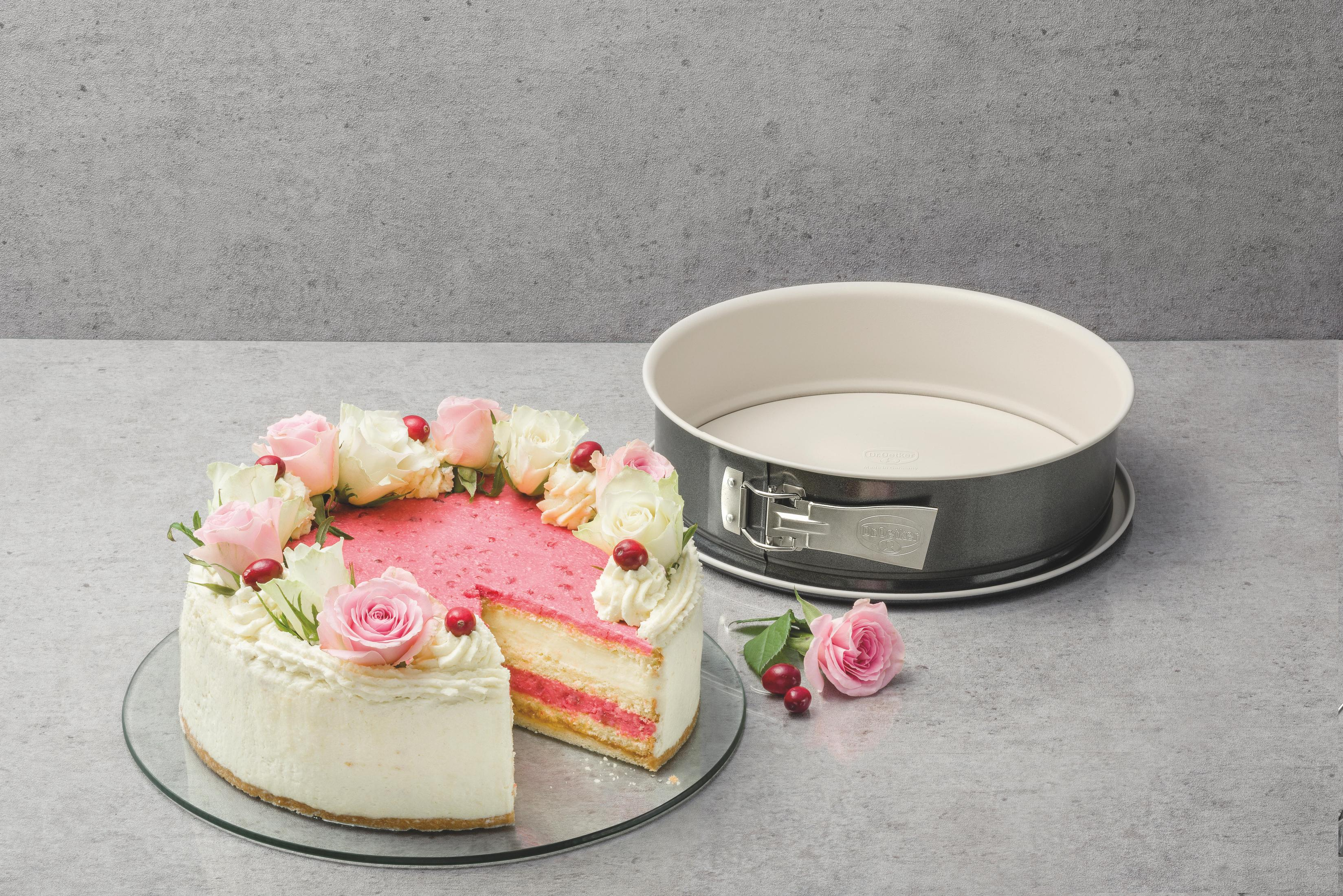 Ein Anschnitt eines Kuchens mit Sahne, Rosen und Beeren neben einer Kuchenform.