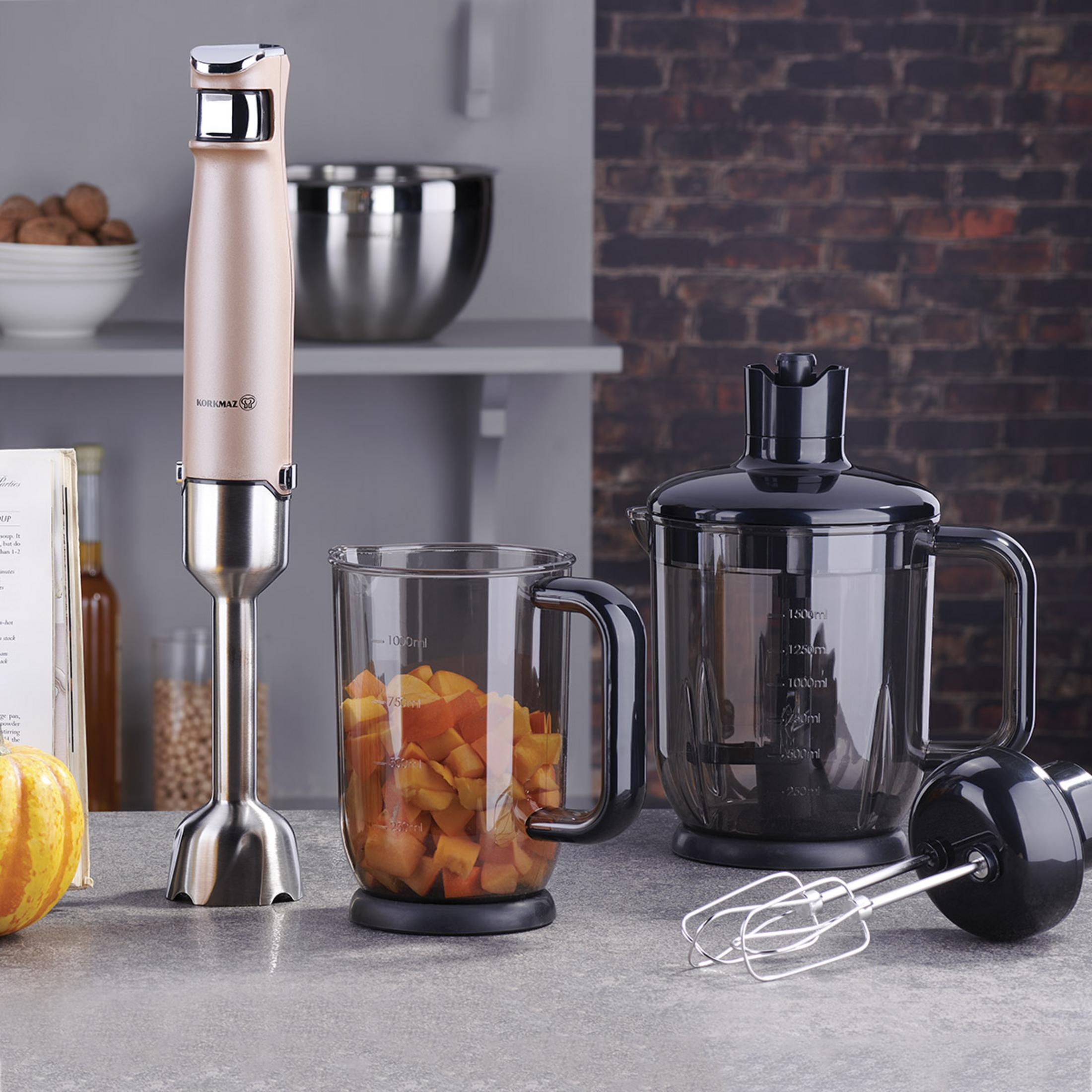 Ein beiger und silberner Stabmixer, ein Glasmessbecher mit gehacktem Kürbis und eine schwarze Küchenmaschine.