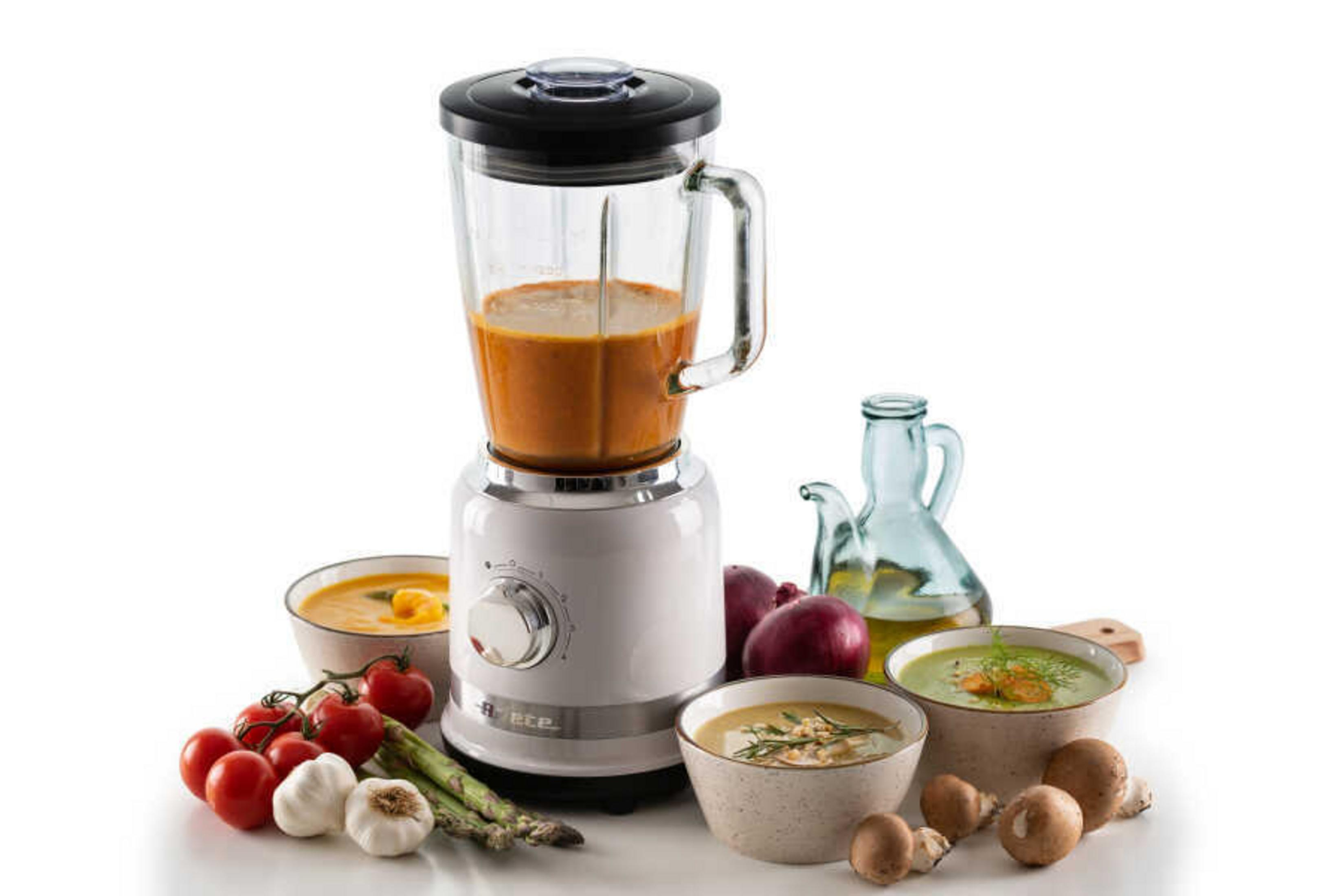 Een witte blender met oranje soep, naast kommen met soep, groenten en champignons.