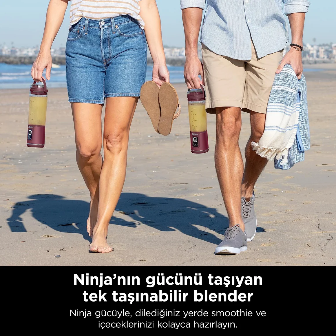 Twee mensen lopen over het strand, elk met een draagbare blender.