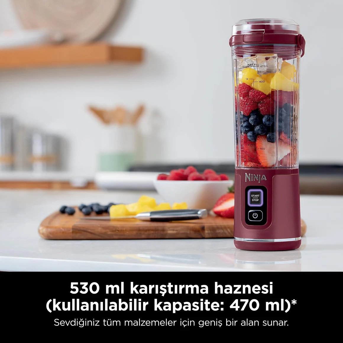 Een rode blender gevuld met fruit staat op een aanrecht. Bessen en ananas ernaast.