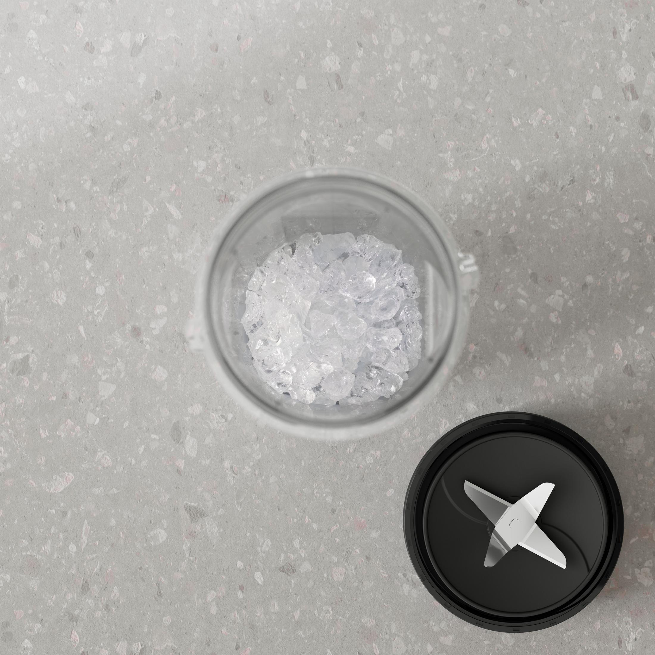 Gri benekli tezgah üzerinde buz dolu bir blender kabının havadan görünümü, yanında siyah kapak ve bıçaklar bulunuyor.