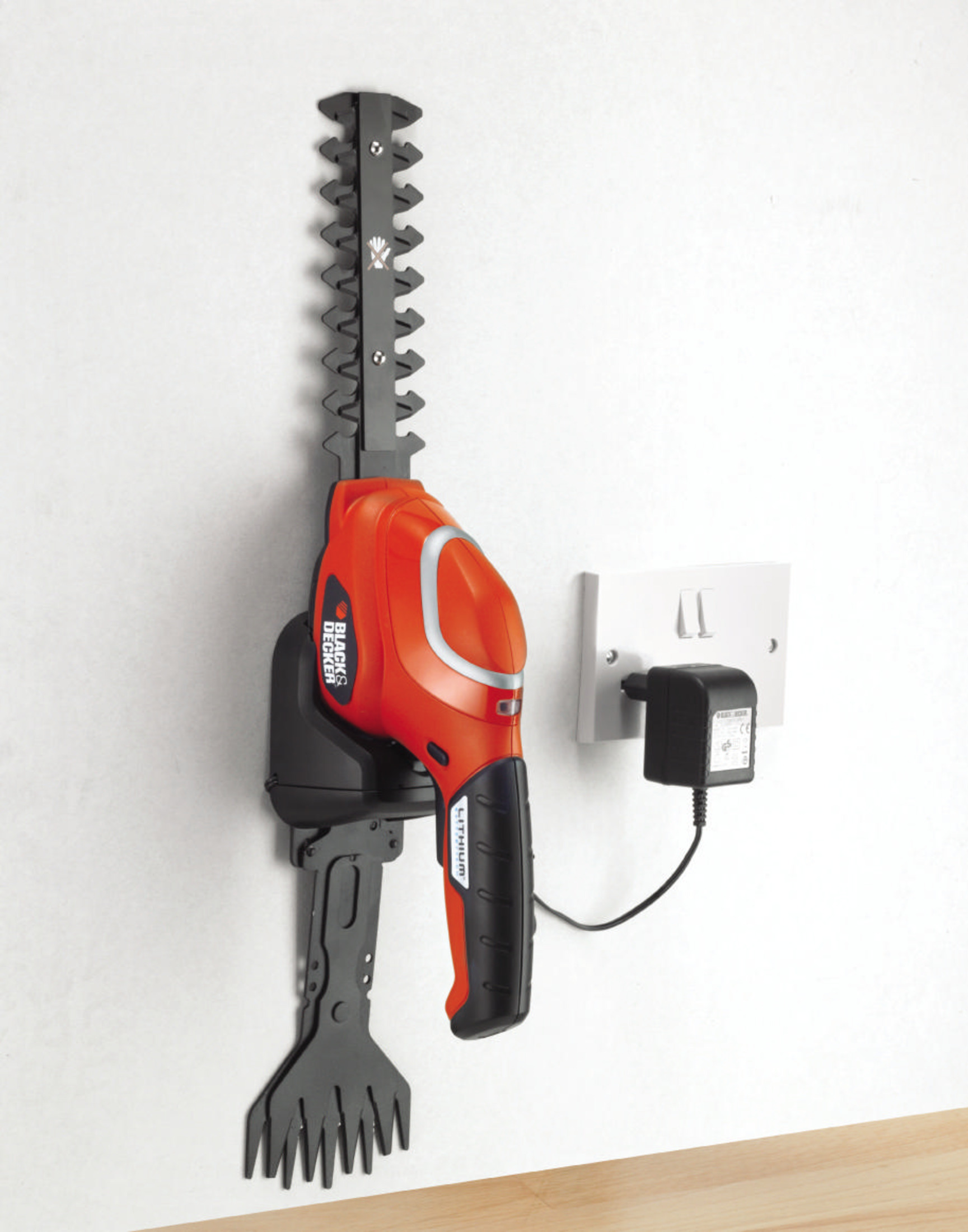 Un cortasetos naranja y negro colgado en la pared, cargando con adaptador.