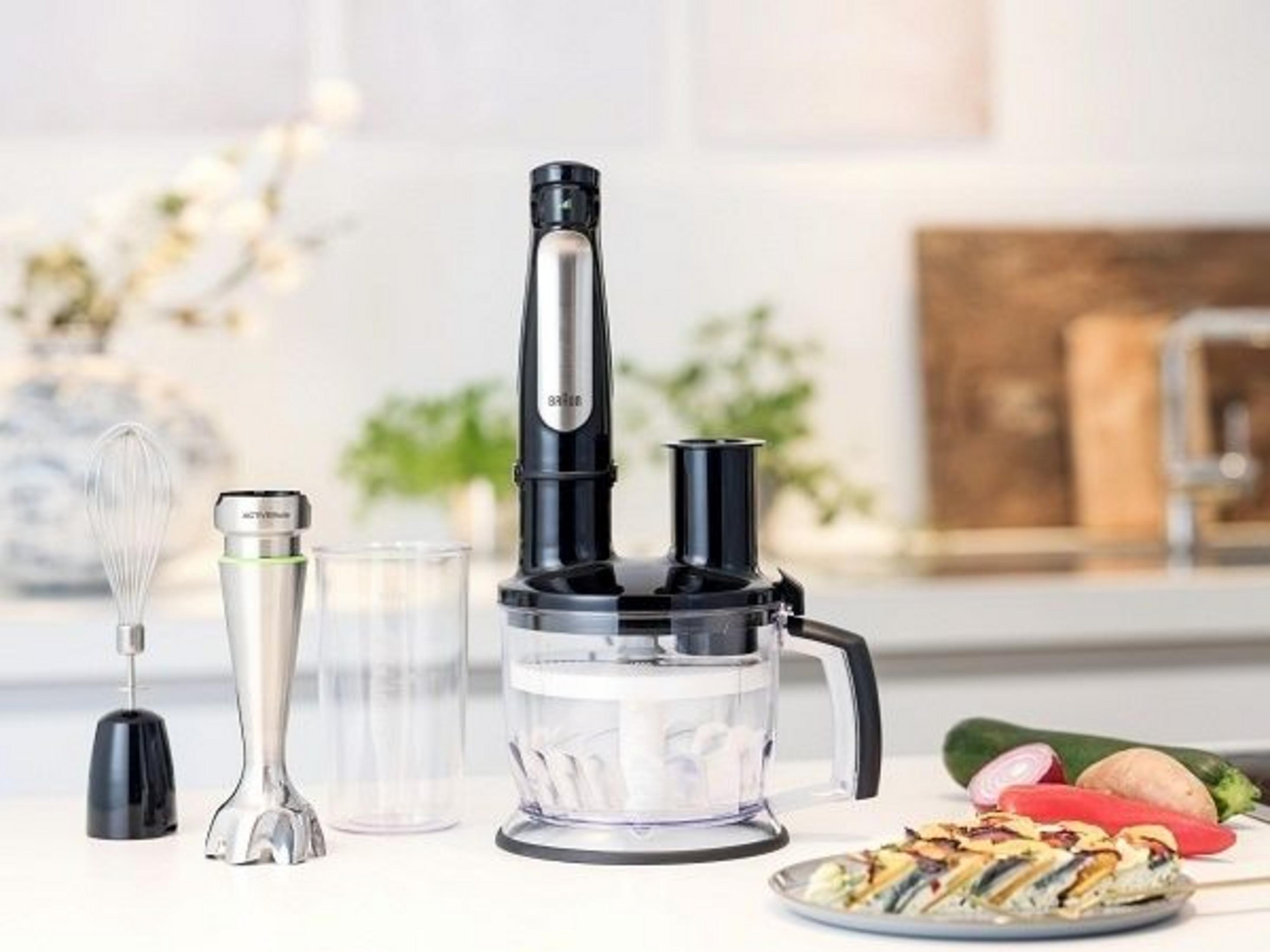 Un set de batidora de inmersión con accesorios, comida y un recipiente en una encimera.