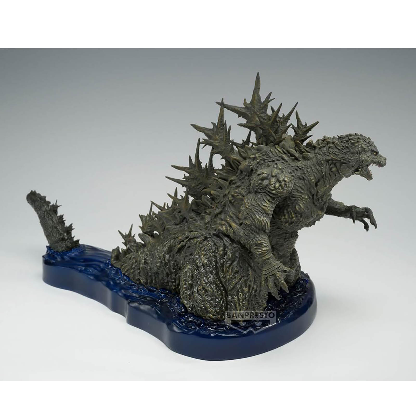 Una dettagliata statuetta di Godzilla, verde scuro e testurizzata, emerge dall'acqua blu su una base blu scuro.