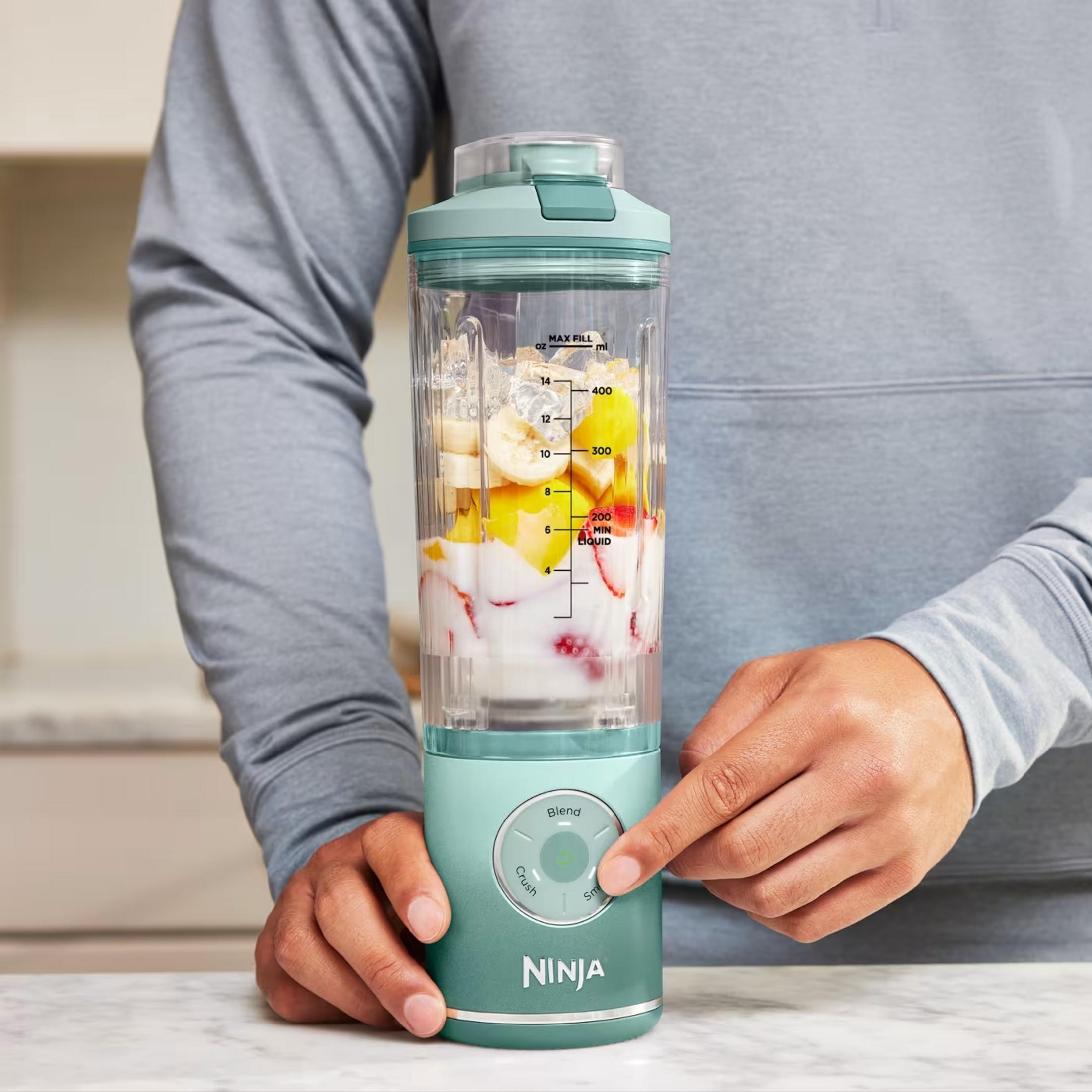 Una persona usa un frullatore Ninja verde menta con frutta e ghiaccio.