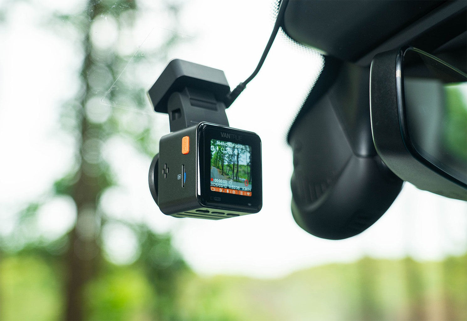 Dashcam mounted on rearview mirror, showing a road view with trees.