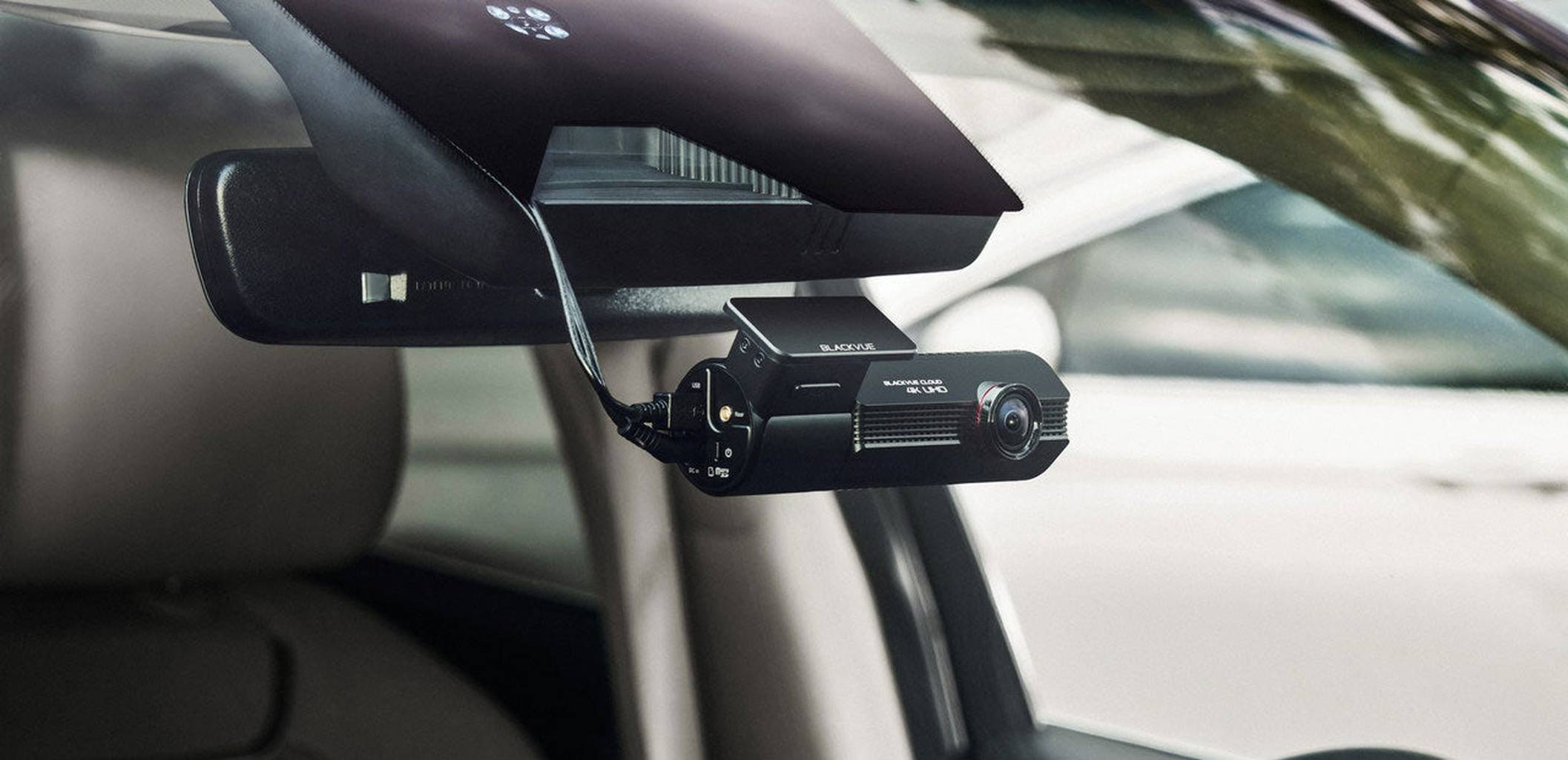 A black car dashcam hangs on the windshield next to the rearview mirror.