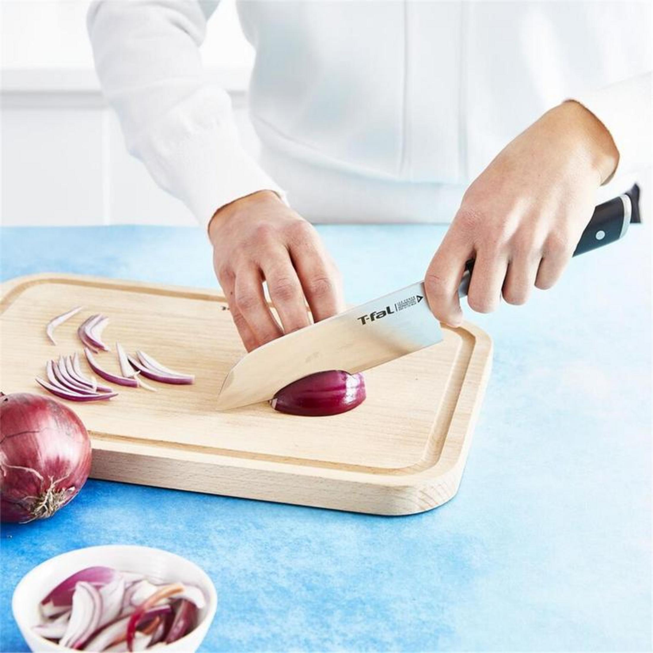 Czerwone cebule są krojone na drewnianej desce. Kilka plasterków leży obok.