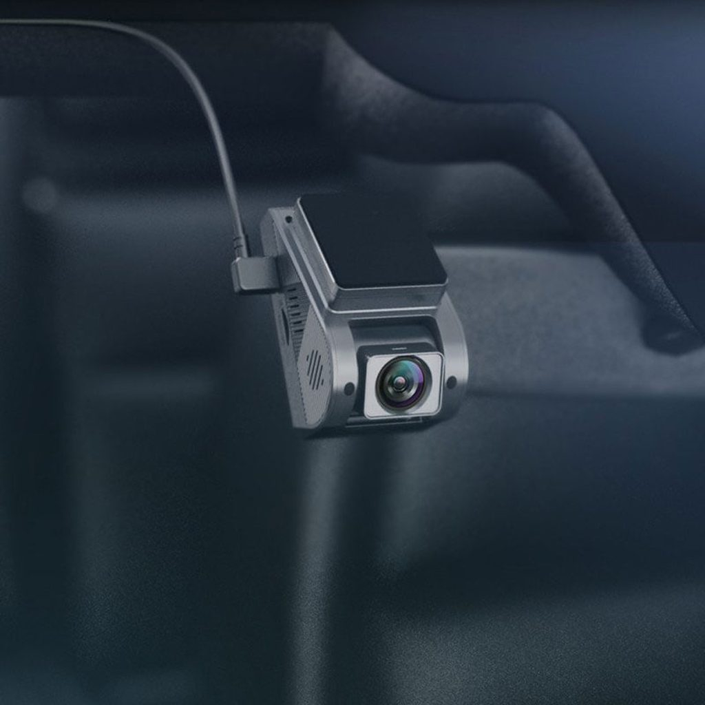 Grijze dashcam met lens, bevestigd aan het autoverlicht.