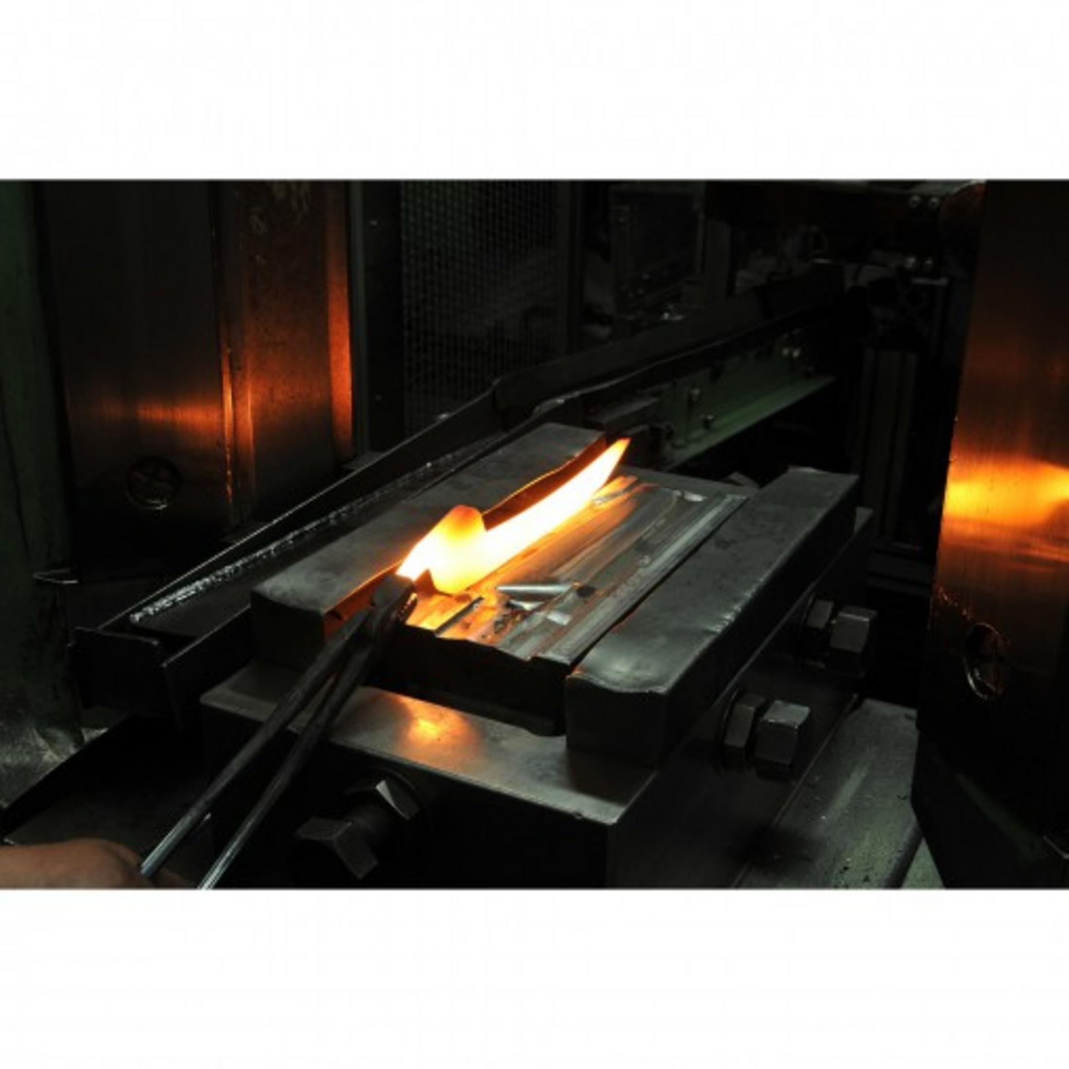 Żarzący się kawałek metalu jest trzymany przez szczypce w warsztacie.