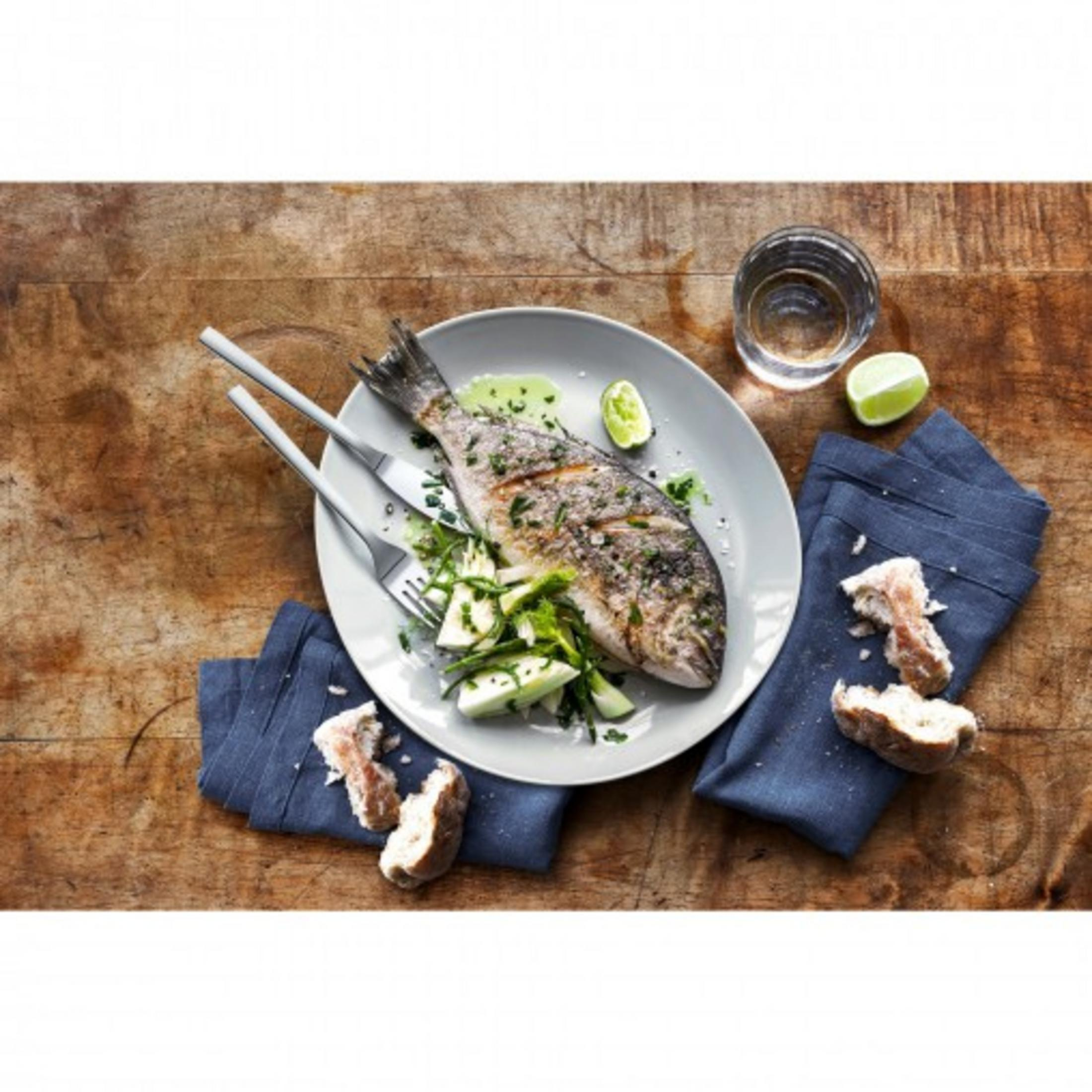 Pesce grigliato su un piatto con limone, erbe e pane.