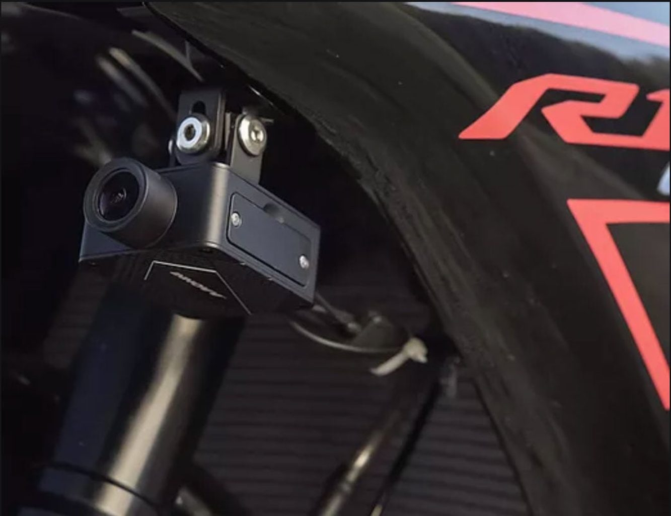 Een kleine zwarte camera is bevestigd aan een motorfiets. Rode accenten zijn zichtbaar.