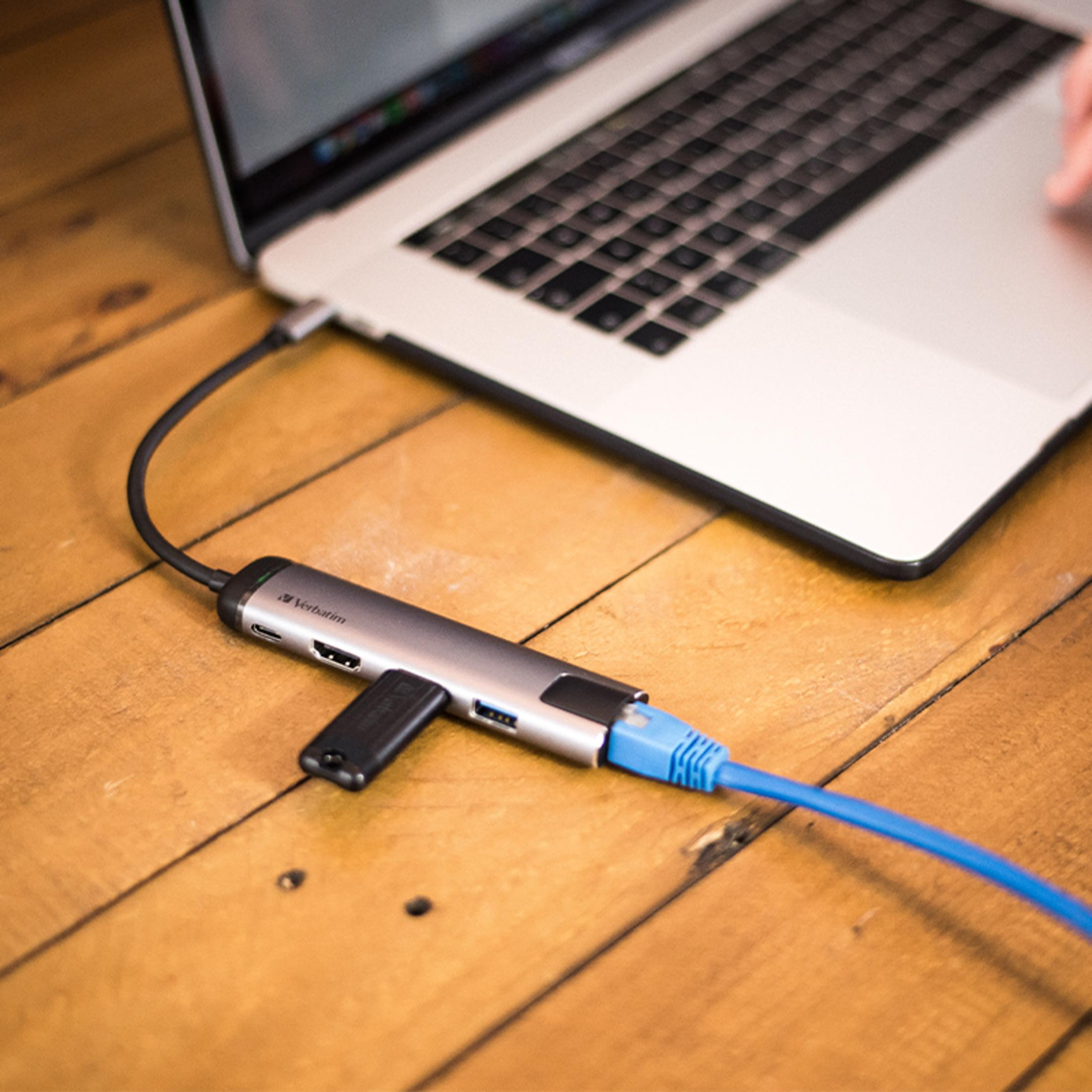 Ein grauer USB-C-Hub mit HDMI, USB und Ethernet-Anschluss, angeschlossen an einen Laptop.