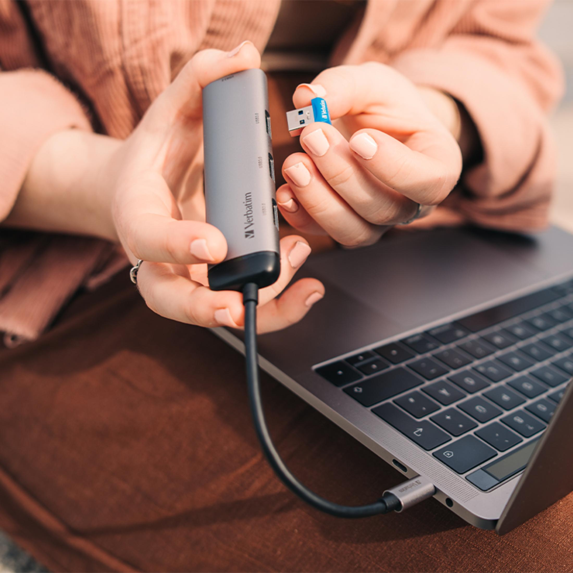 Una persona tiene un hub USB-C e un'unità USB accanto a un laptop.