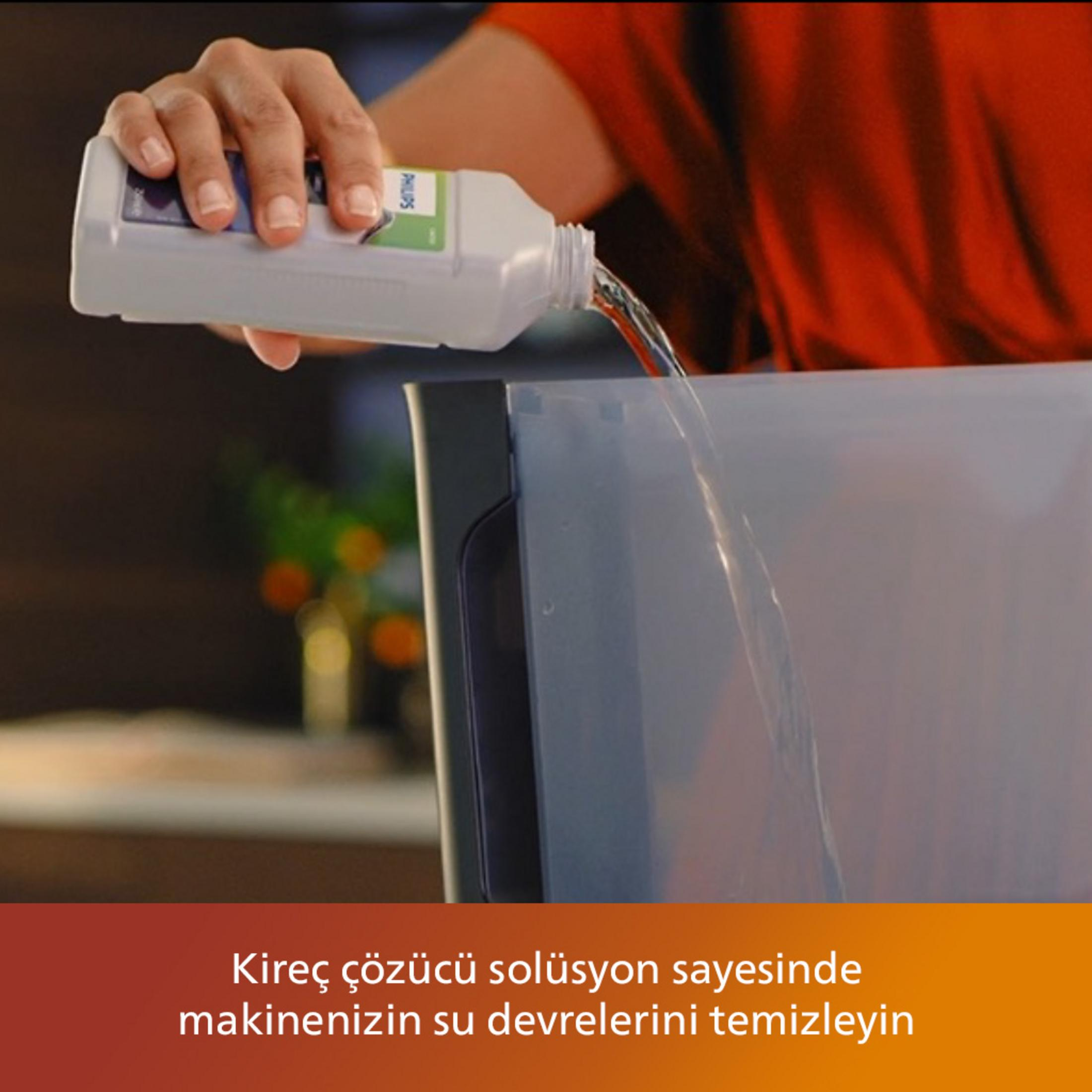 Eine Hand gießt Flüssigkeit aus einer weißen Flasche in einen grauen Behälter.