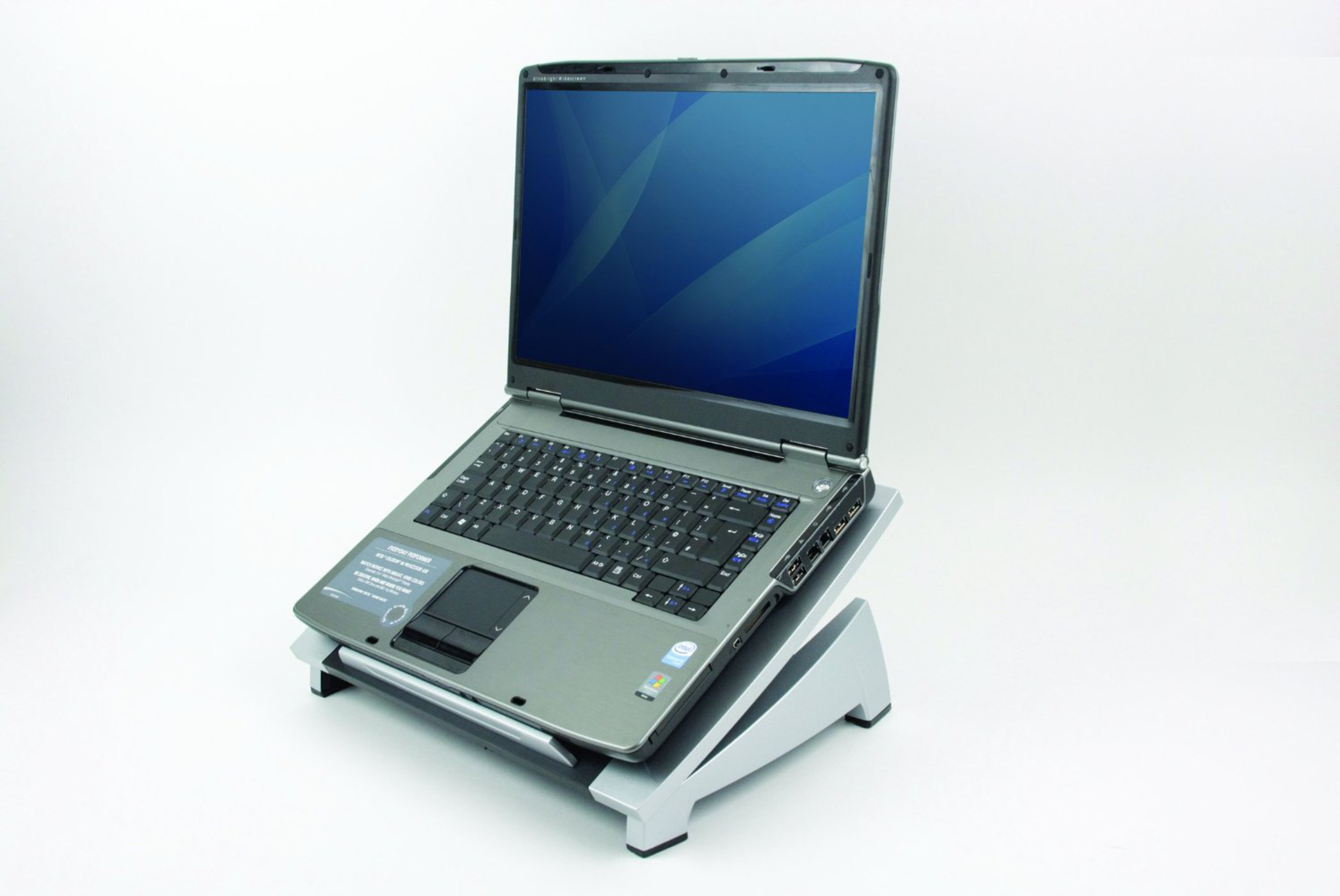 Ein grauer Laptop mit blauem Bildschirm, der ein grafisches Design zeigt, steht schräg auf einem silbernen Ständer vor weißem Hintergrund.