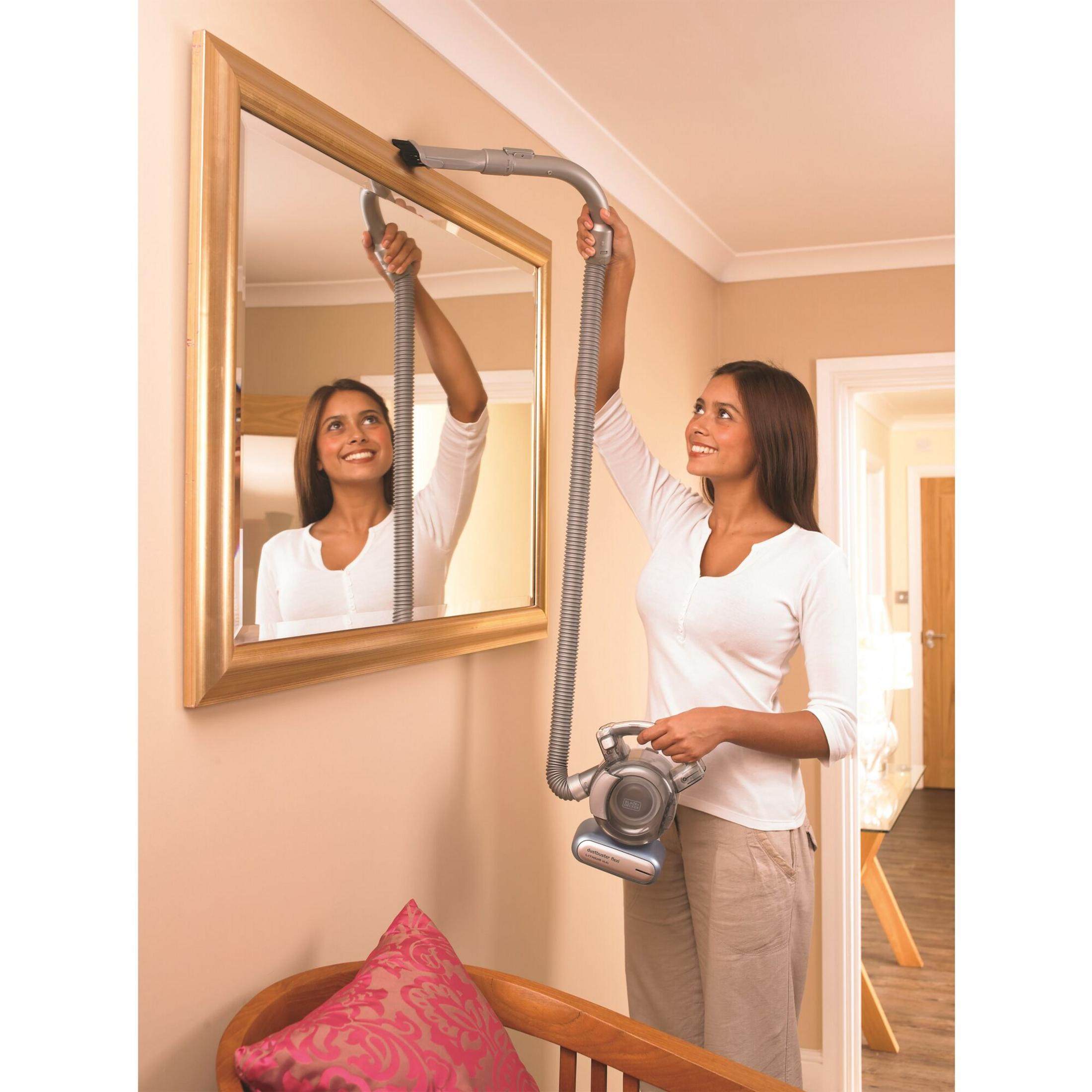 Une femme passe l'aspirateur sur le dessus d'un cadre de miroir.